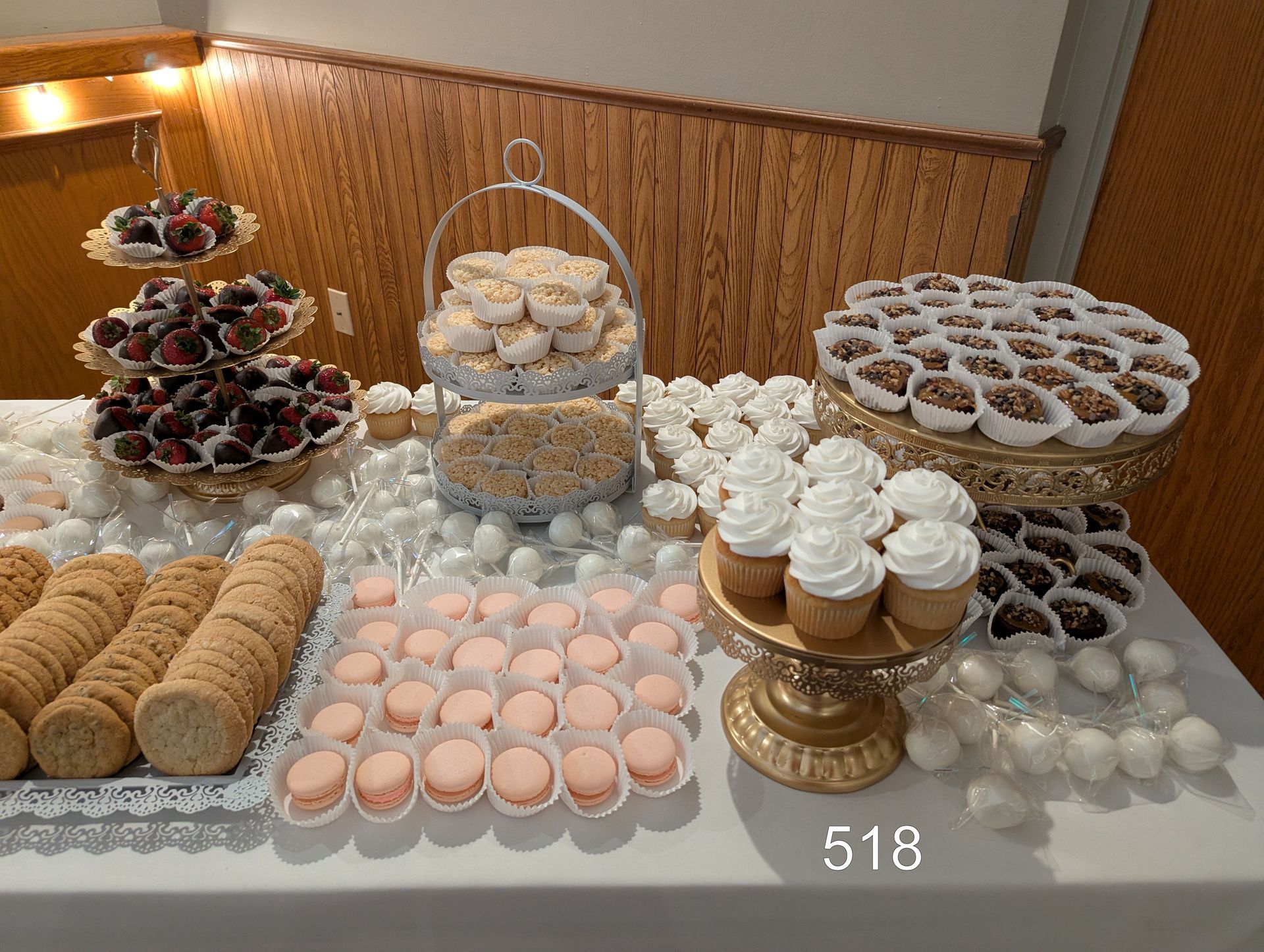 Dessert buffet with assorted cookies, cupcakes, macarons, and sweets arranged on trays and stands