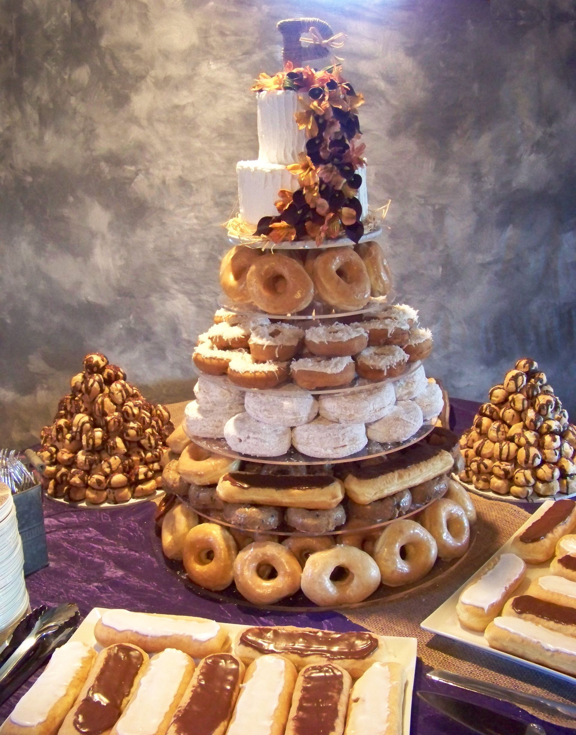 Tall dessert tower of donuts, pastries, and sweets on a table with purple cloth and smoky backdrop