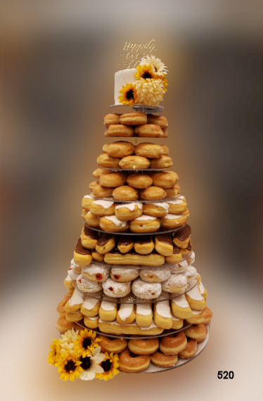 Tower of assorted donuts stacked into a cone, topped and accented with yellow flowers.