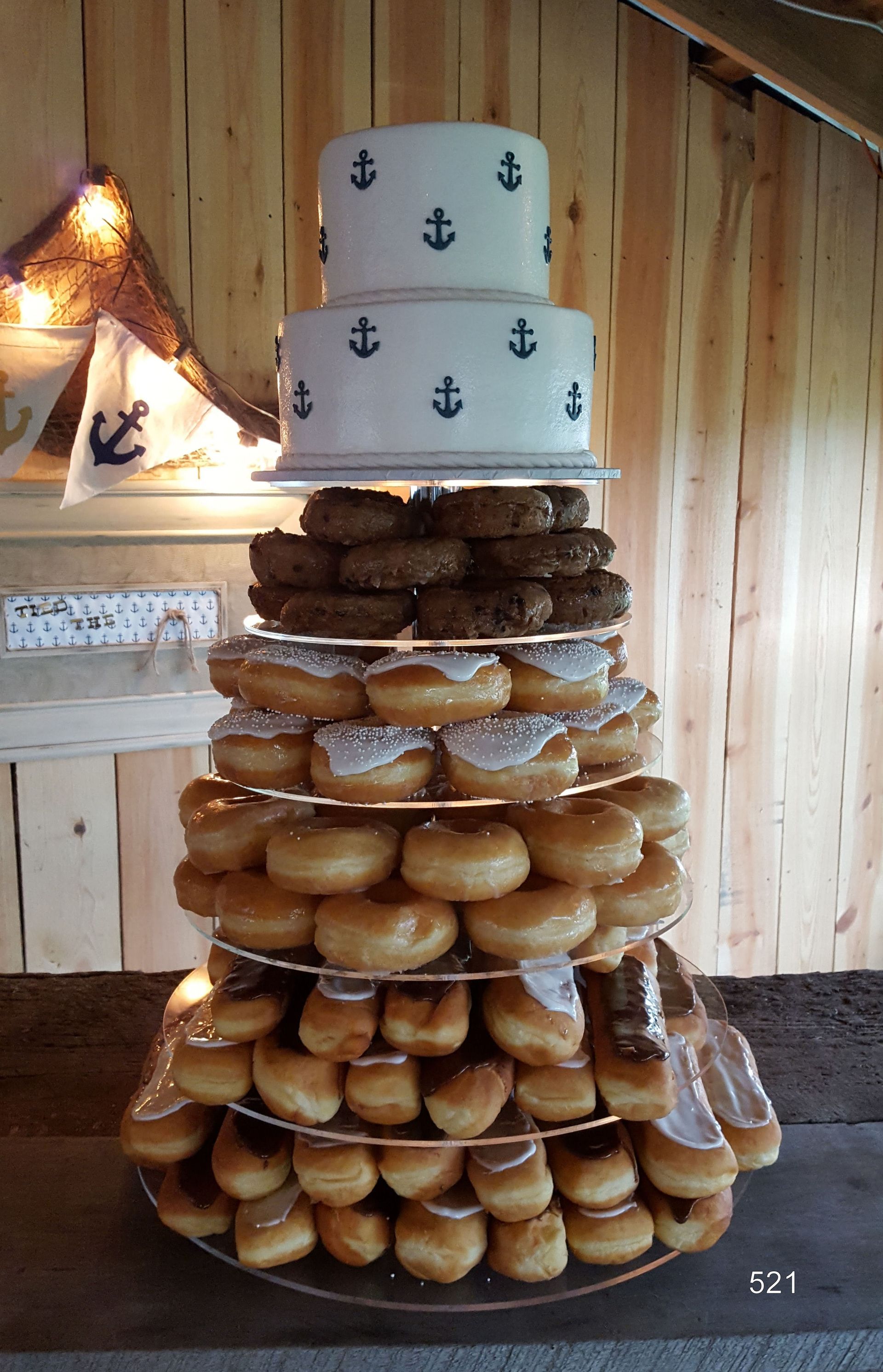 A stacked doughnut cake with two white top tiers decorated with anchors in a rustic wooden room.