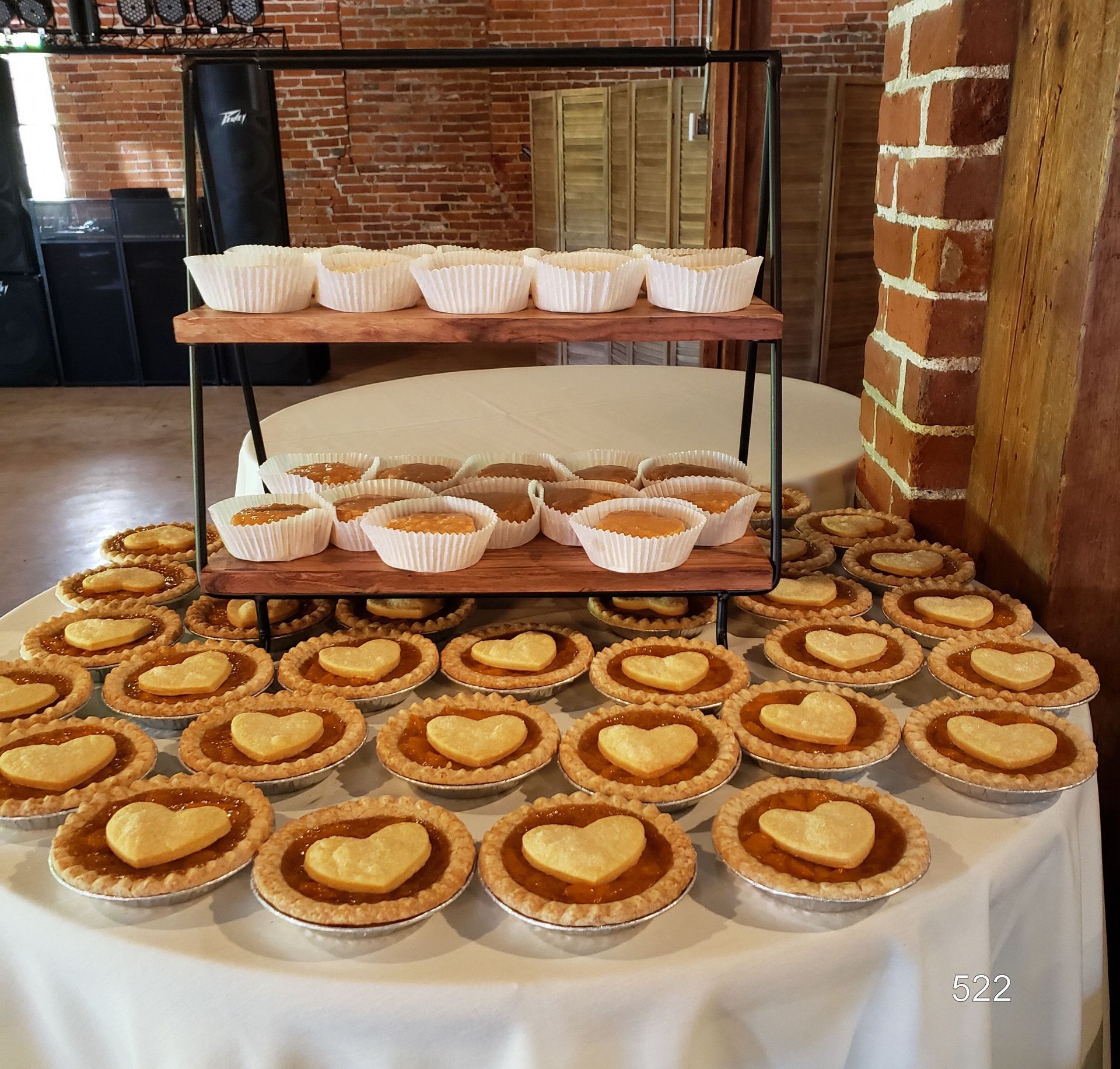 Dessert table with rows of mini tarts and pie bars on a white tablecloth and metal shelf rack