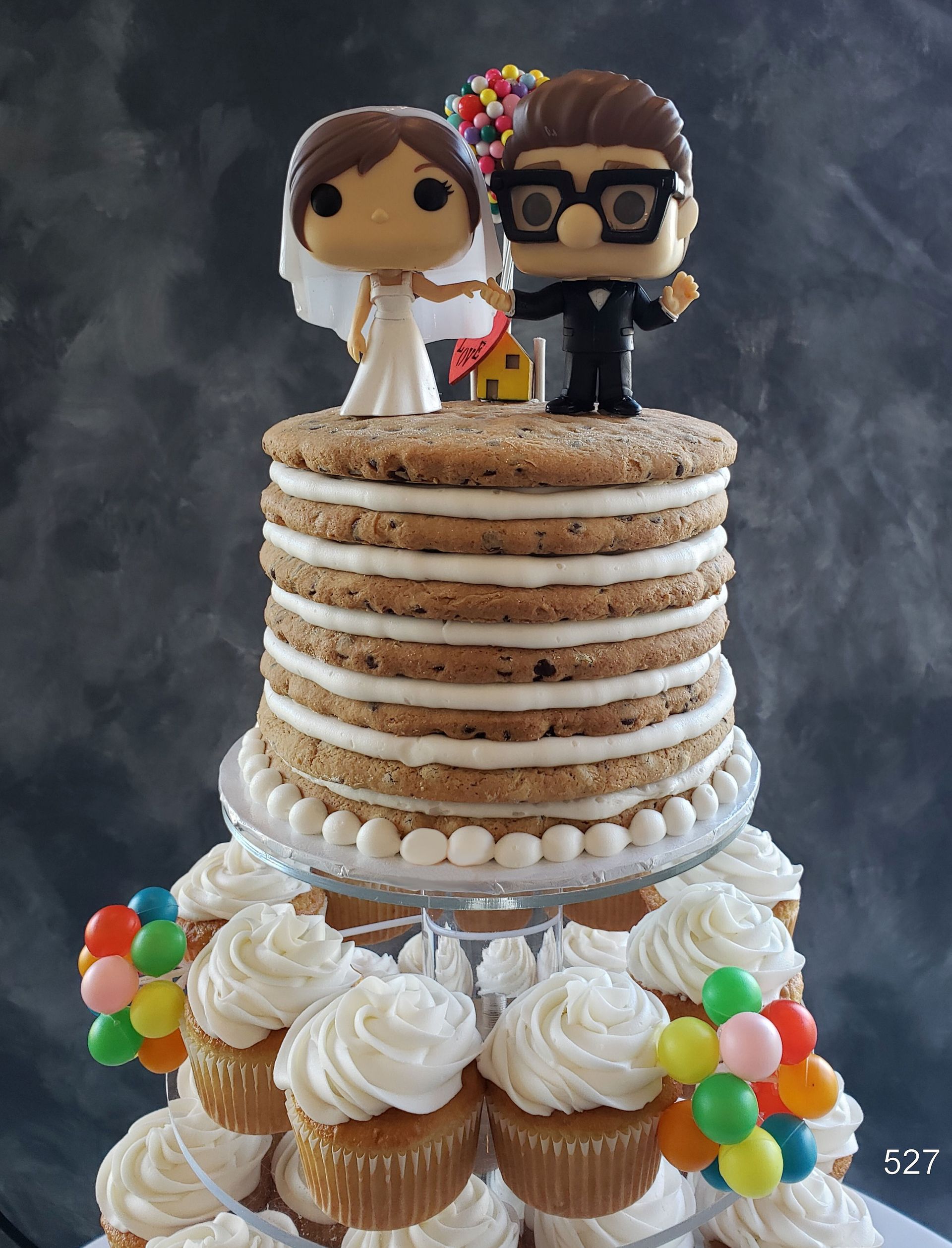 Wedding cake topped with bride and groom figurines, decorated with white frosting and colorful balloons