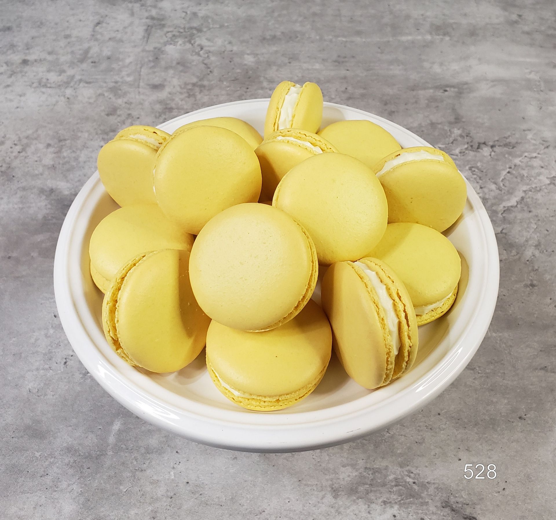 Yellow macarons piled in a white bowl on a gray countertop