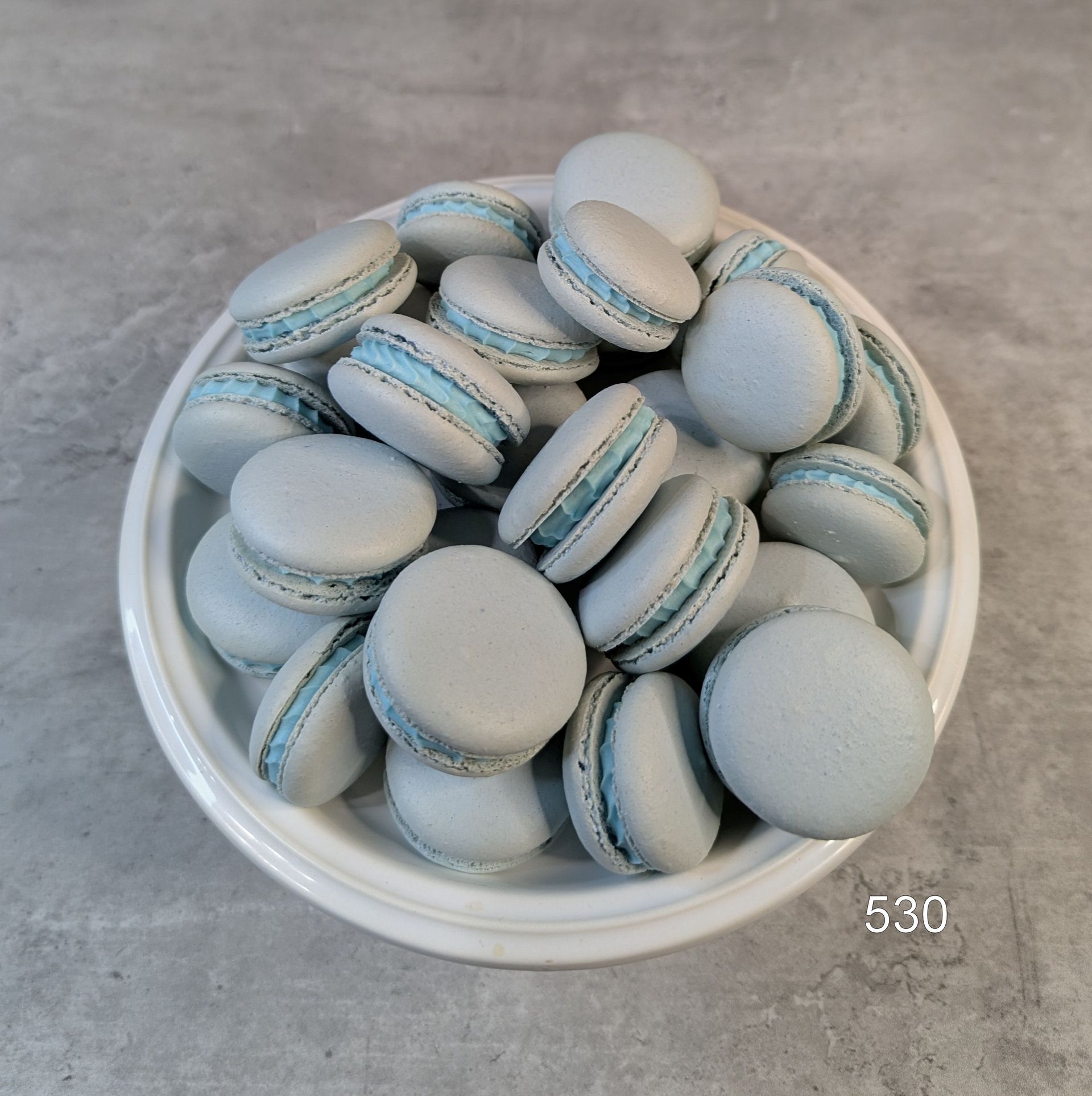 White bowl filled with light blue and white macarons on a gray surface