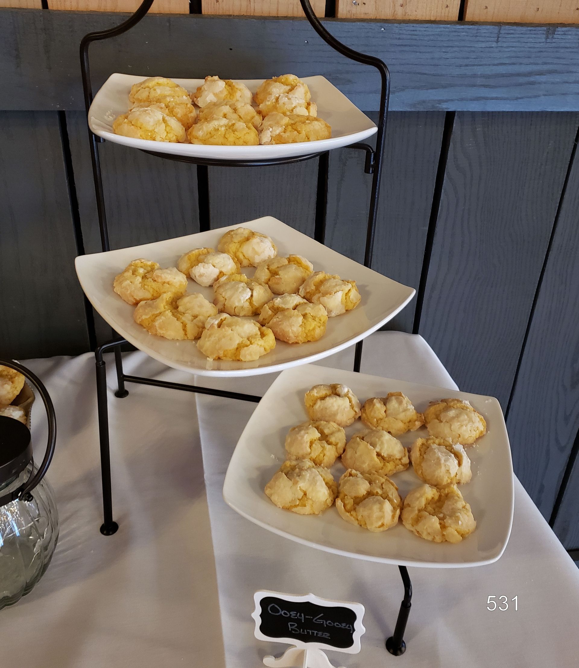 Three-tier dessert stand with powdered donut holes on white plates in a rustic display.