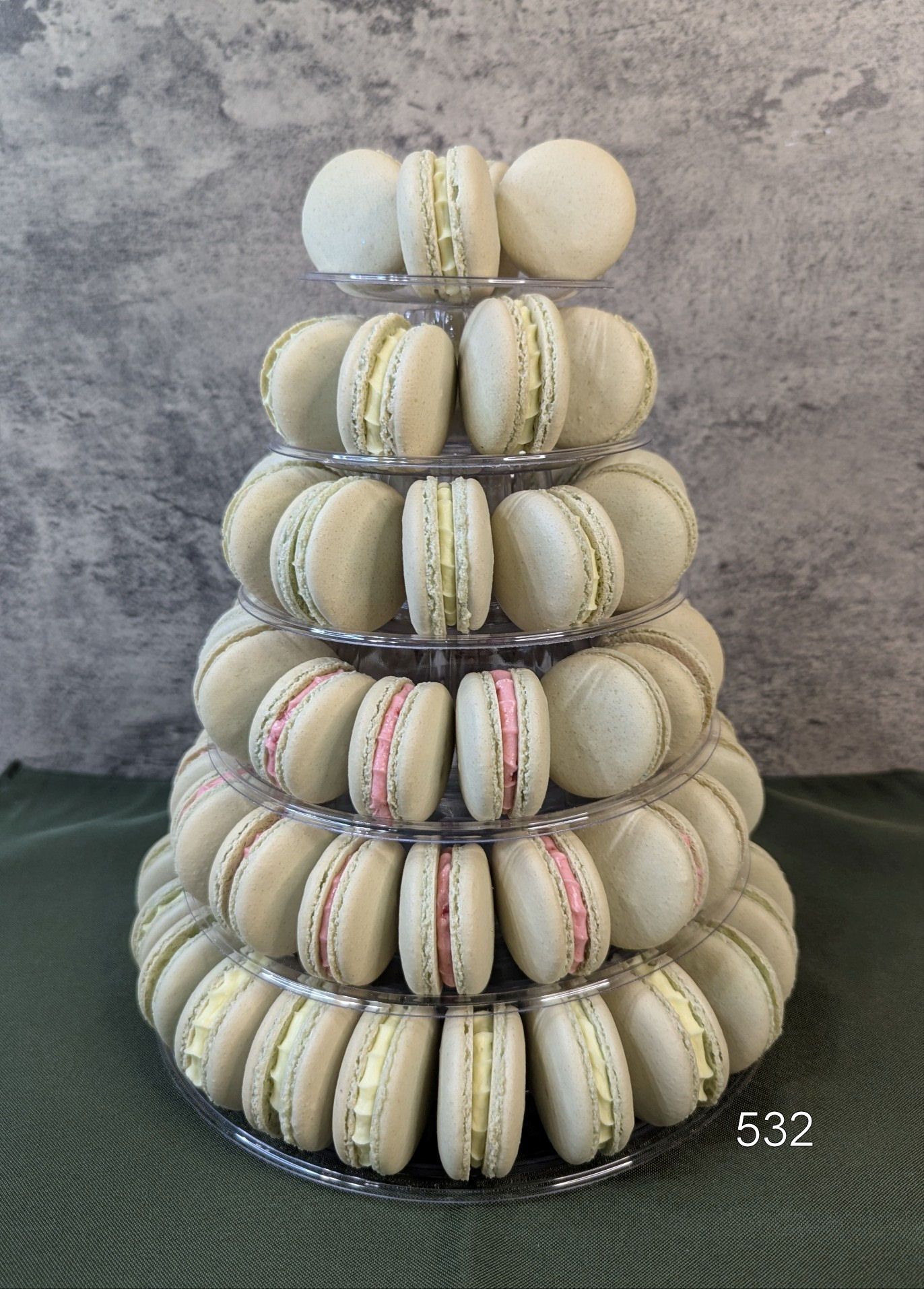 Pyramid of stacked macarons in cream, beige, and pink on a dark green cloth against a gray background
