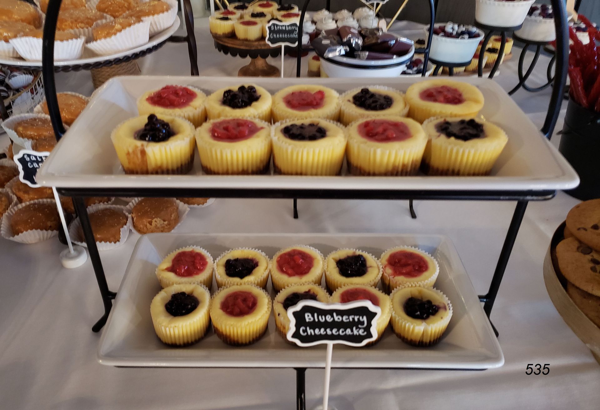 Tiered dessert stand with vanilla and blueberry cheesecakes topped with berries at a buffet