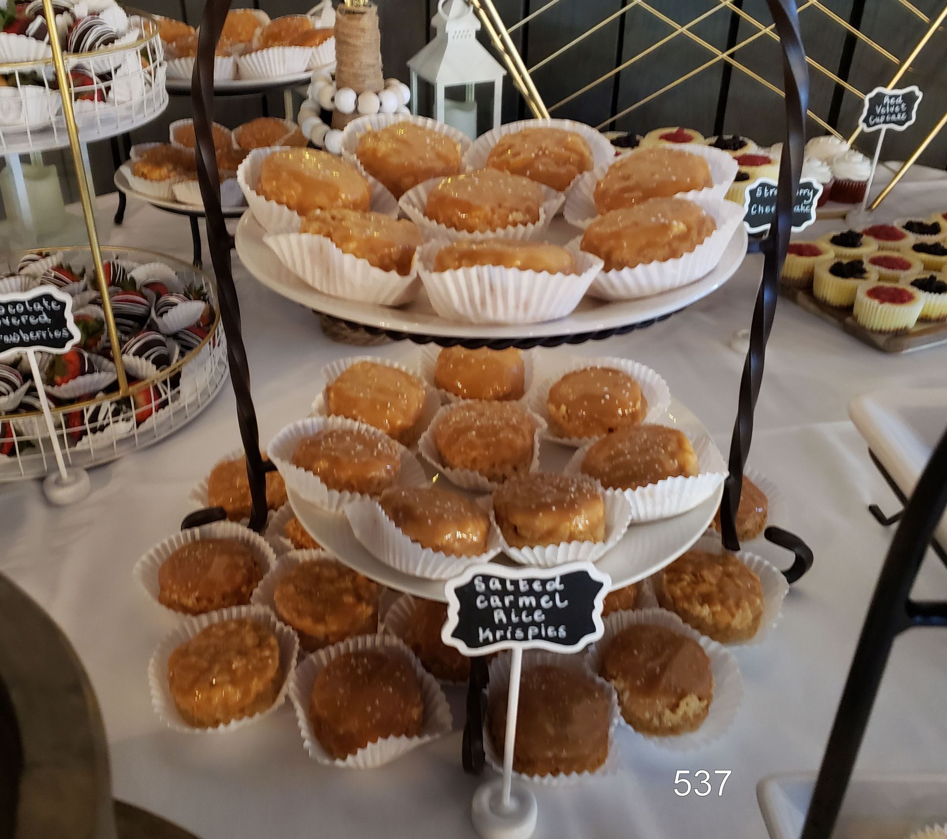 Tiered tray of glazed doughnuts and muffins at a dessert table with small chalkboard labels