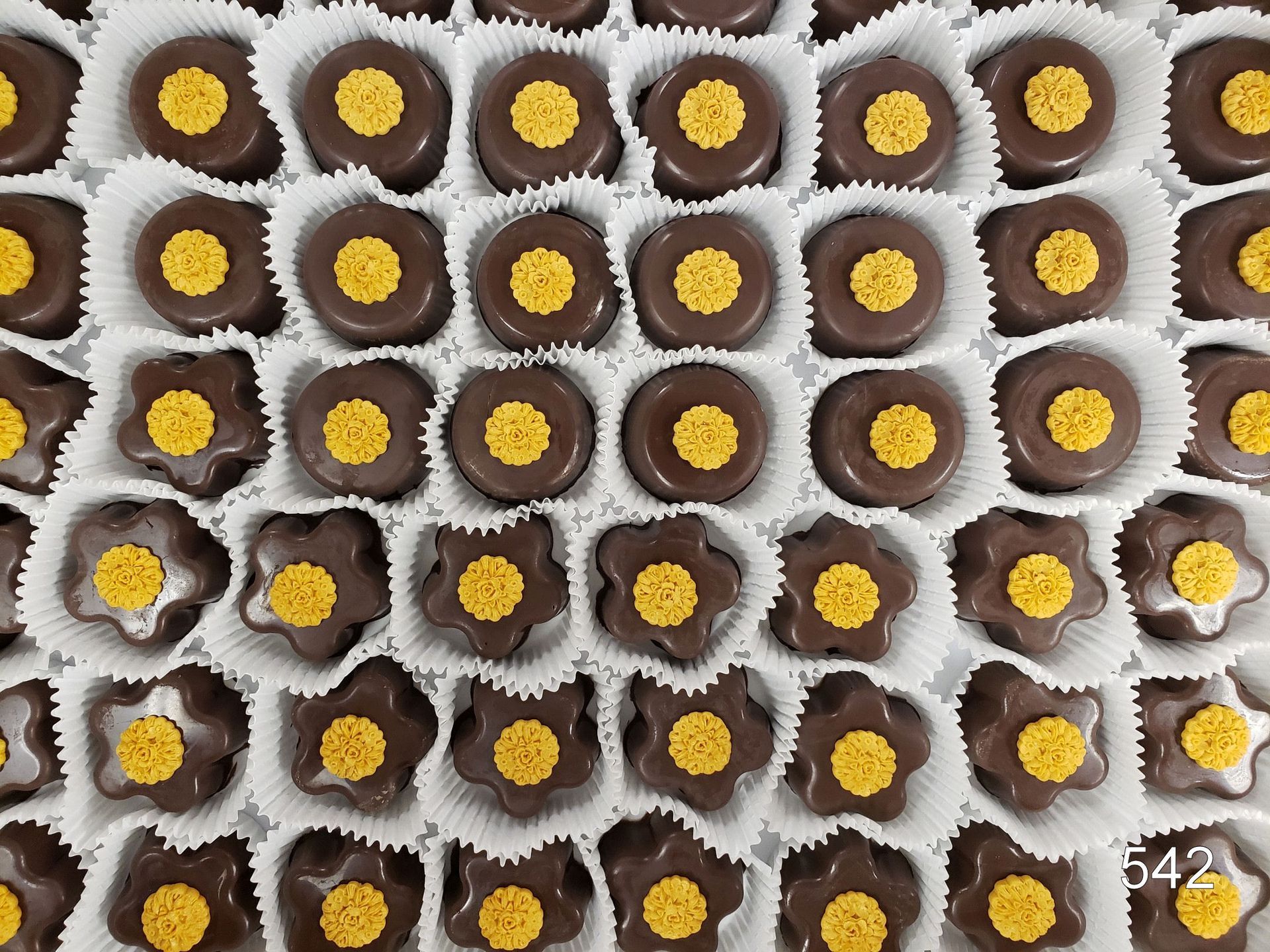 Rows of chocolate and yellow candy treats in white paper cups, viewed from above