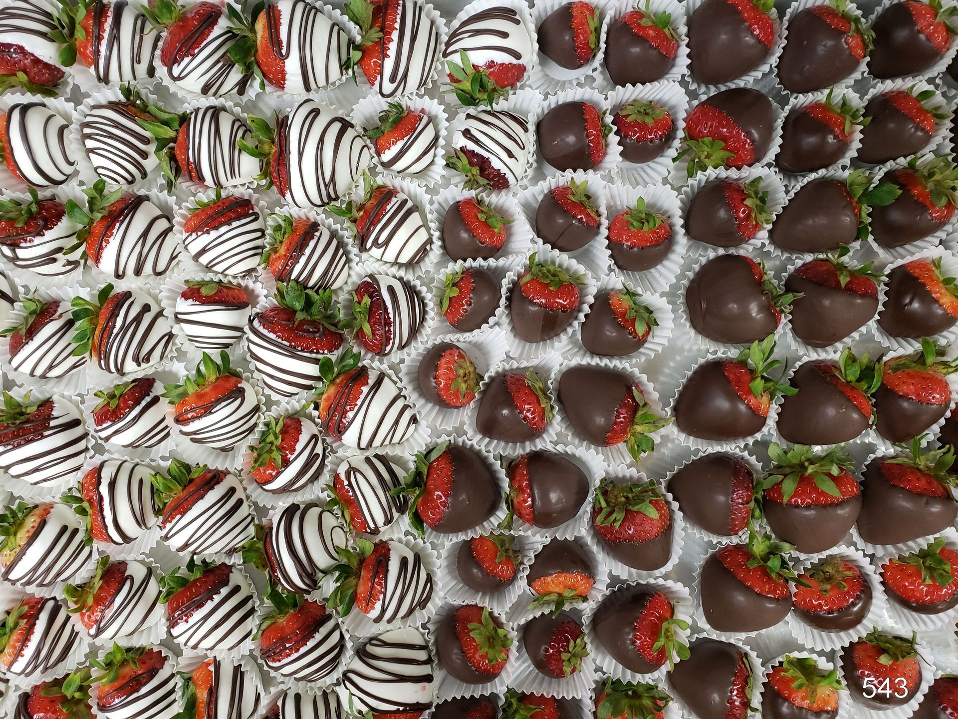 Assorted chocolate-covered strawberries with white and dark drizzle arranged in rows.