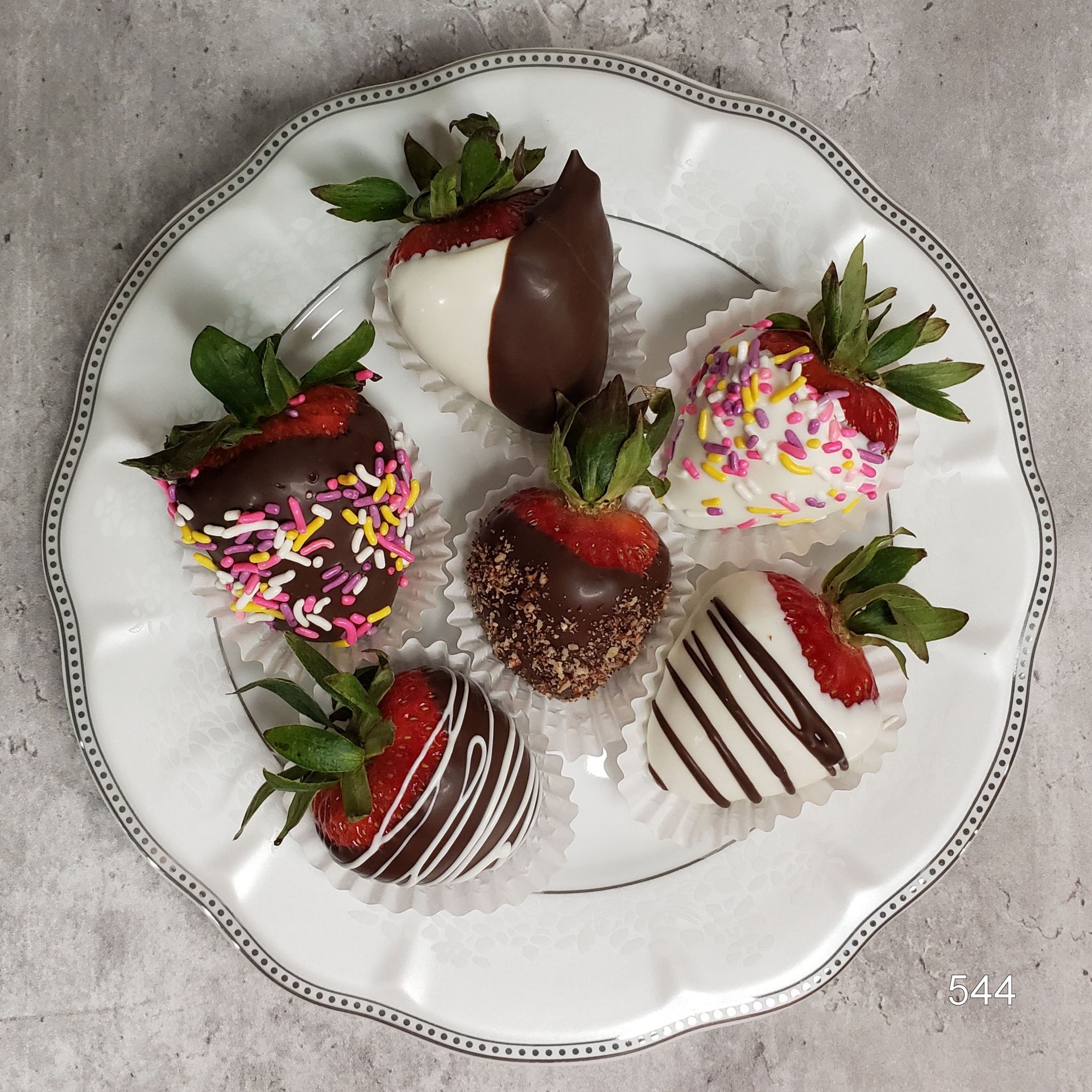 White plate of chocolate-dipped strawberries, some drizzled and sprinkled with colorful toppings.