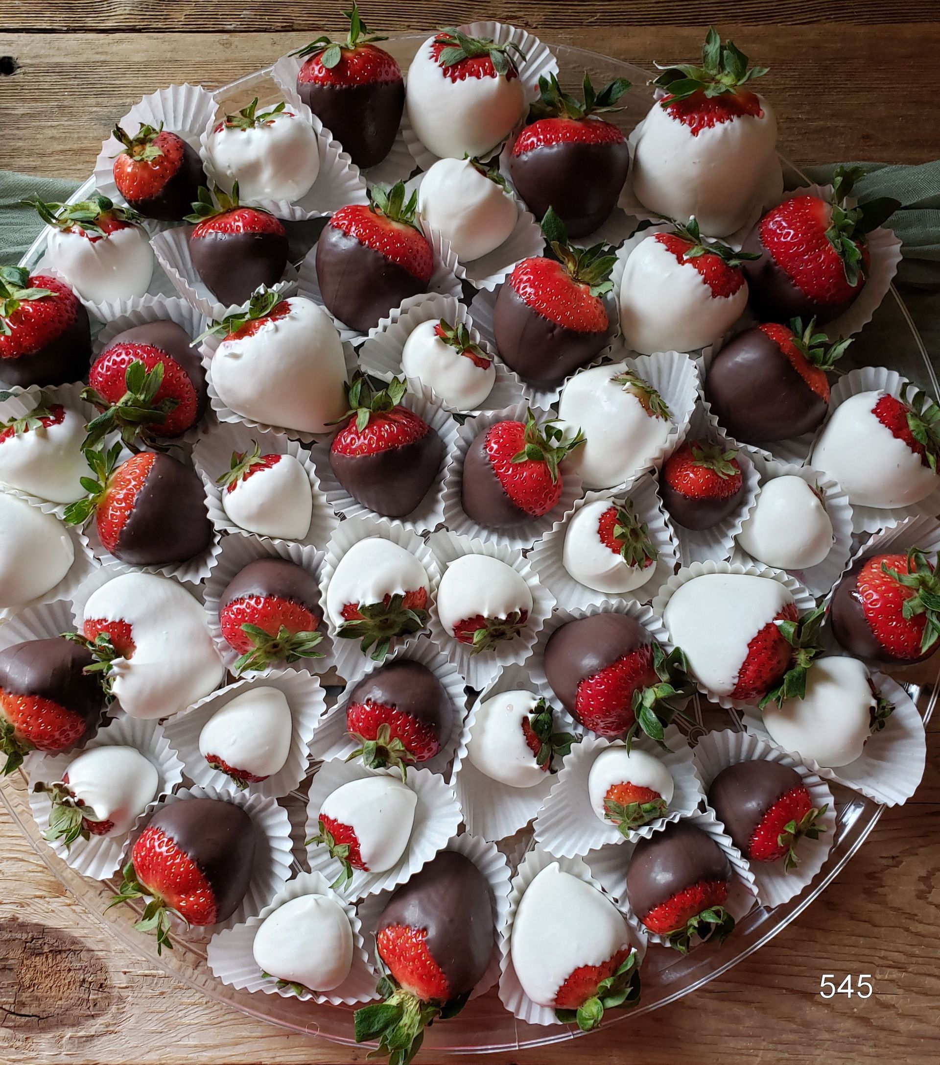 Tray of chocolate-dipped strawberries topped with white drizzle on a wooden table.