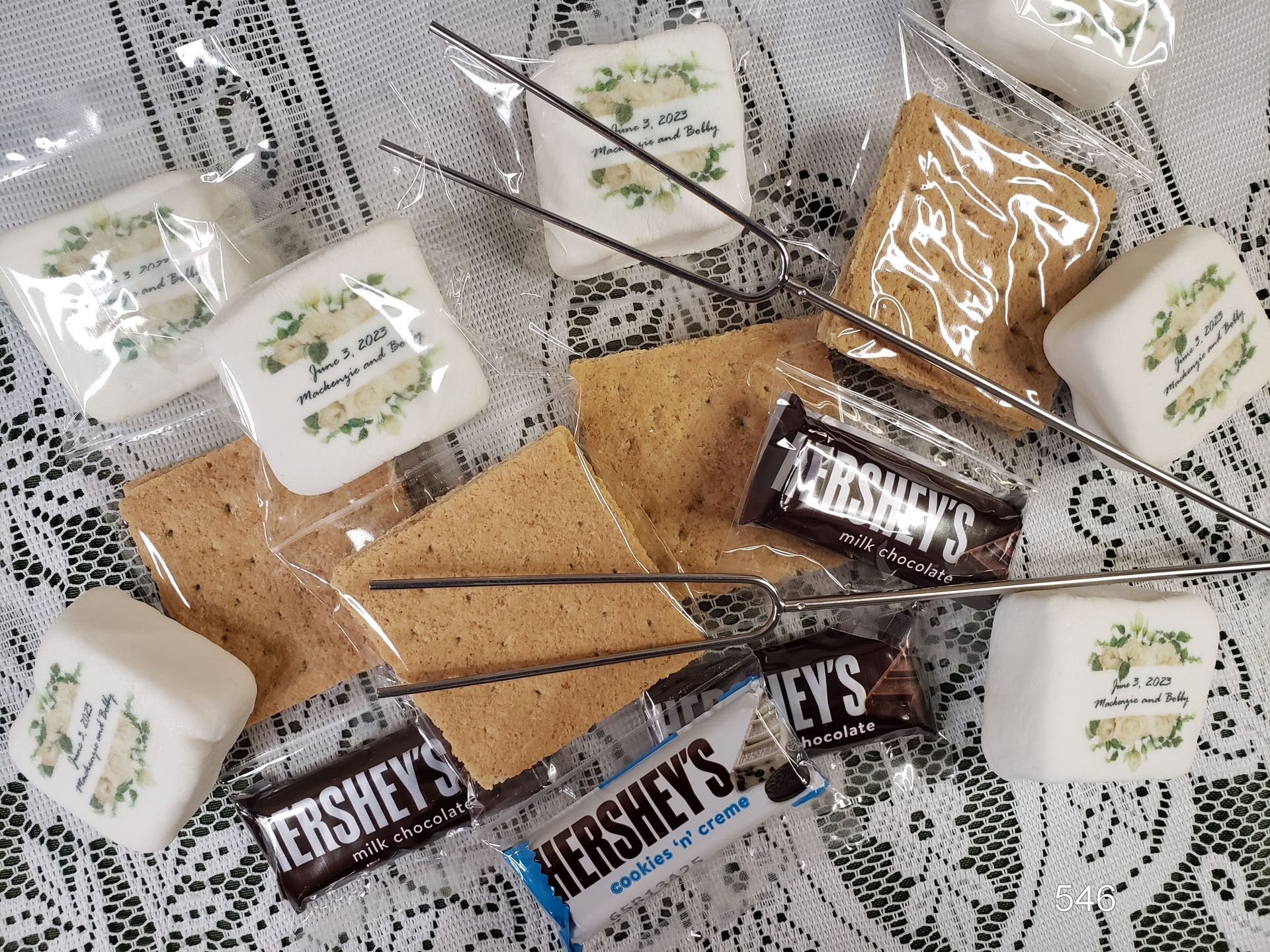 S’mores ingredients on a lace tablecloth, with graham crackers, Hershey’s chocolate, and marshmallows.