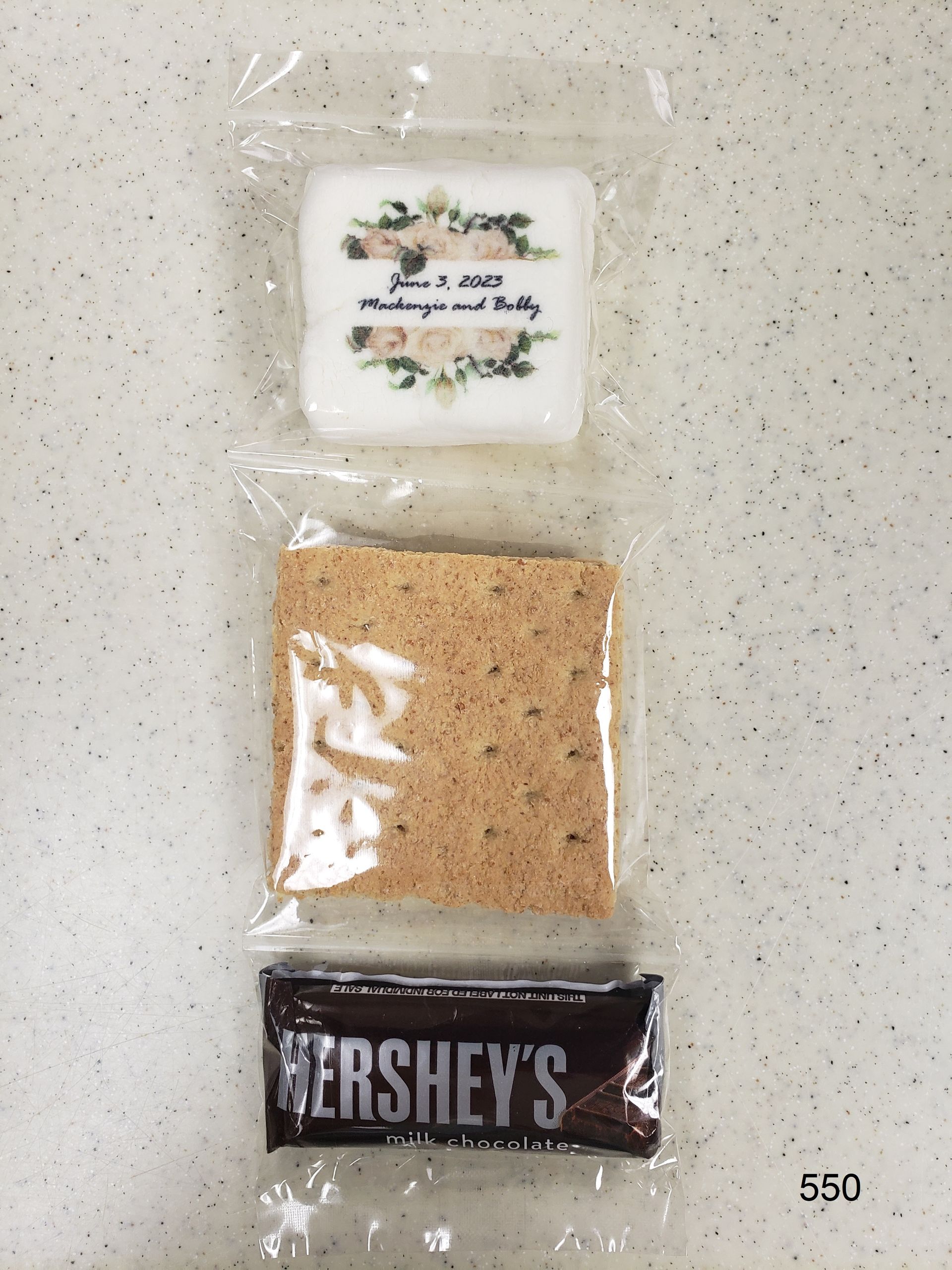 Three packaged items on a speckled countertop: a white-labeled pouch, a tan bag, and a Hershey’s bar.