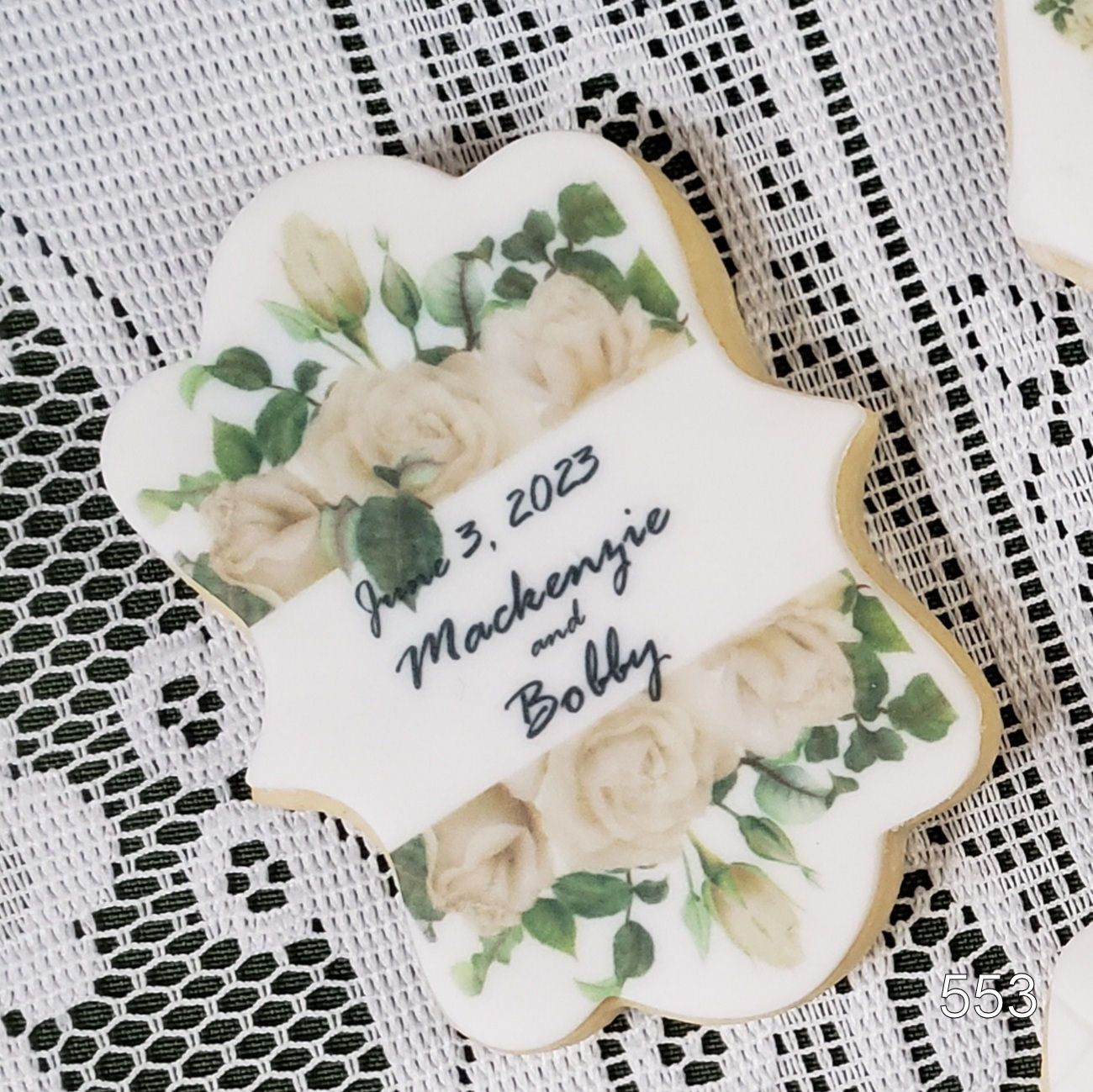 White floral plaque with green leaves on lace, reading “June 2023 Machinery Baby.”
