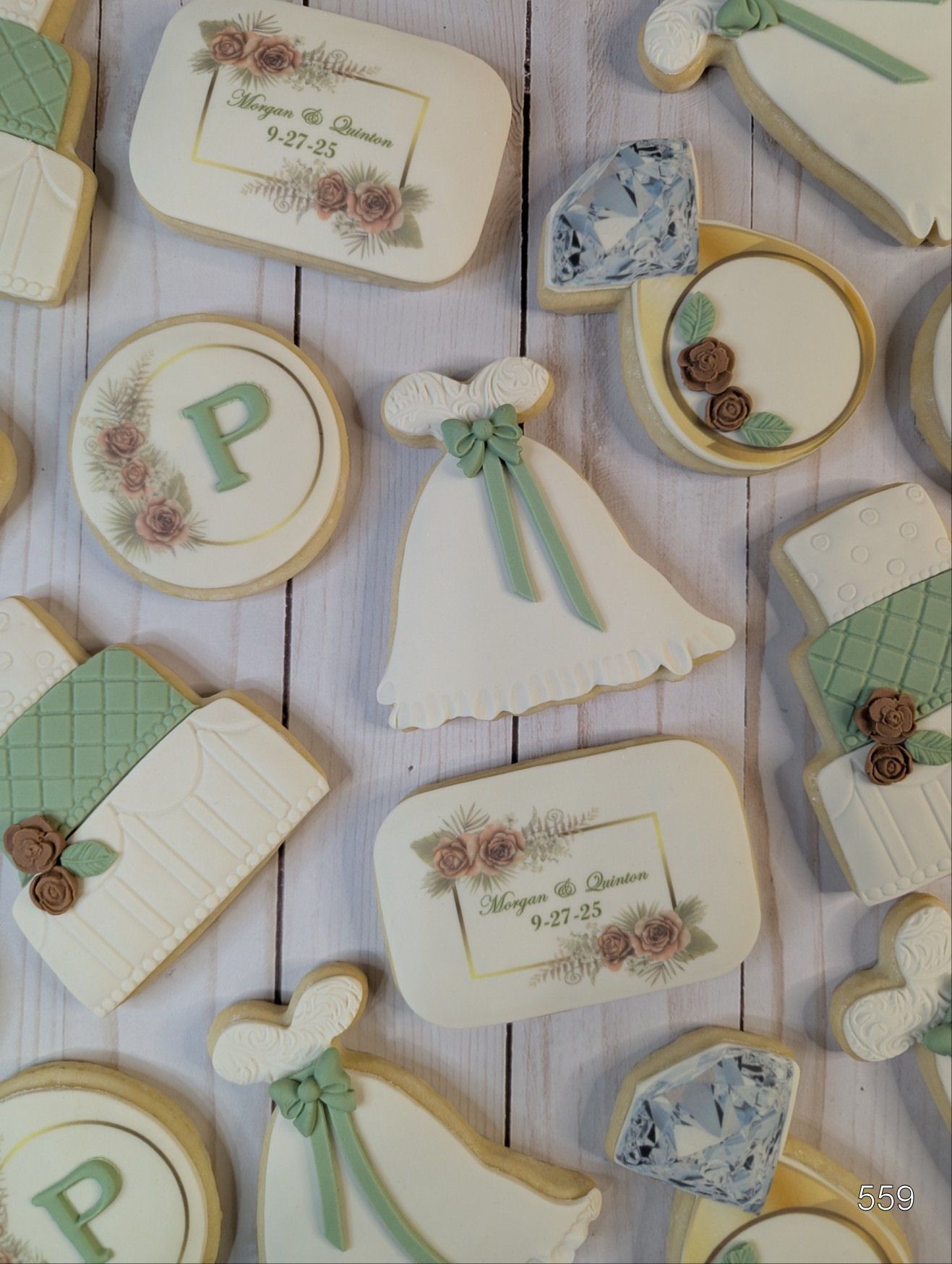 Pastel decorated cookies with bows, flowers, and monogram letters arranged on a white cloth.