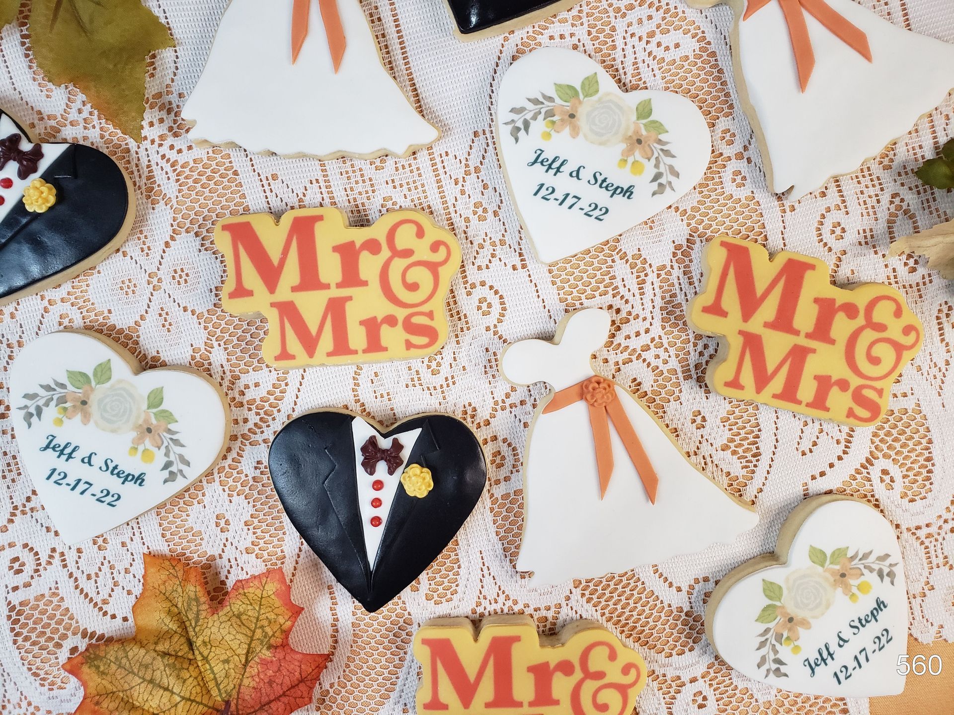 Wedding-themed decorations with “Mr & Mrs” signs, autumn leaves, and a heart-shaped tuxedo cutout on white lace.