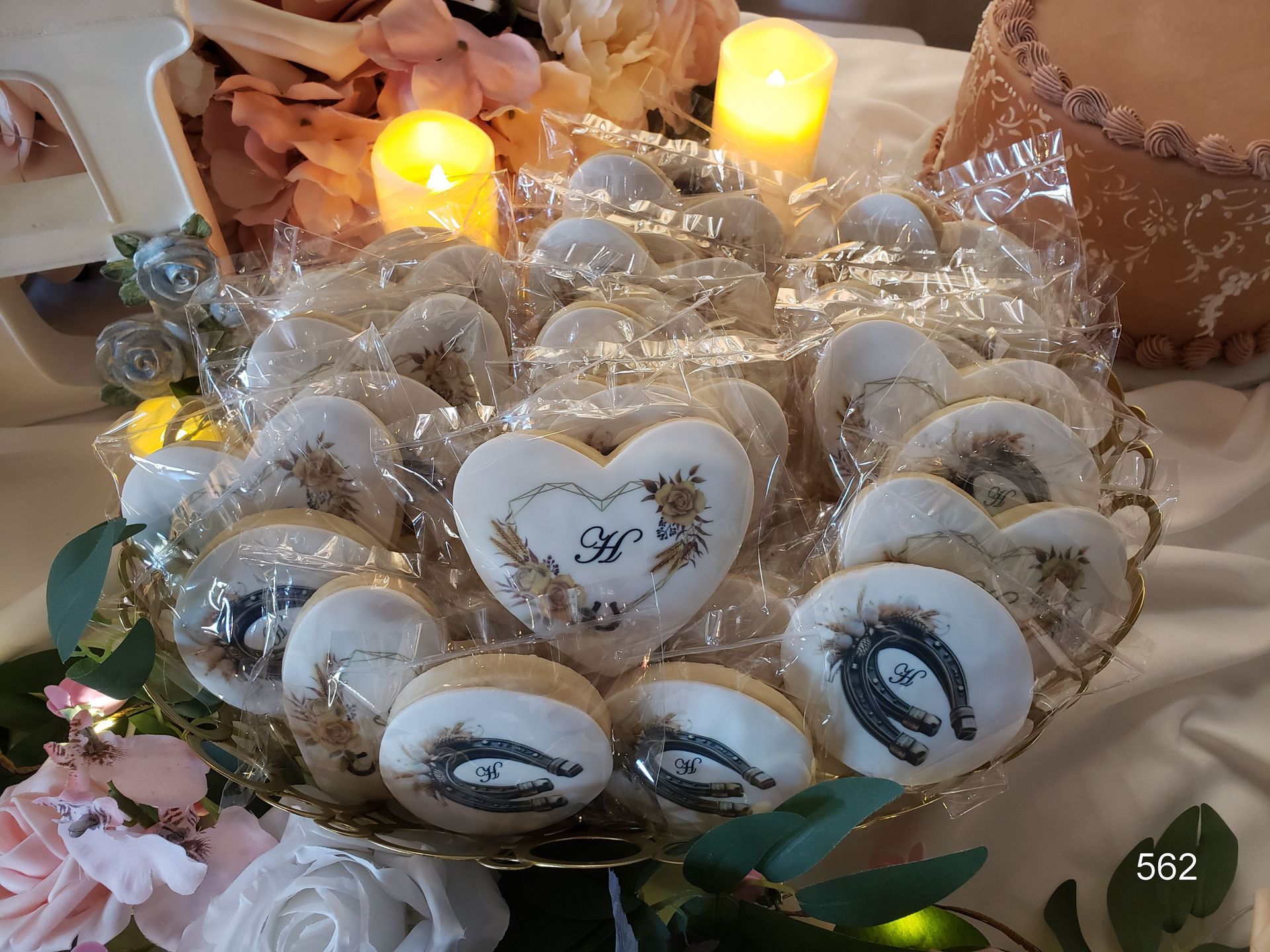 Heart-shaped tray of decorated cookies with candles on a table, wrapped in clear cellophane with pink flowers.
