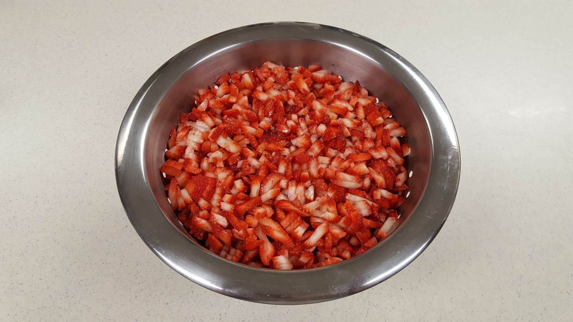 a metal bowl filled with chopped strawberries on a counter