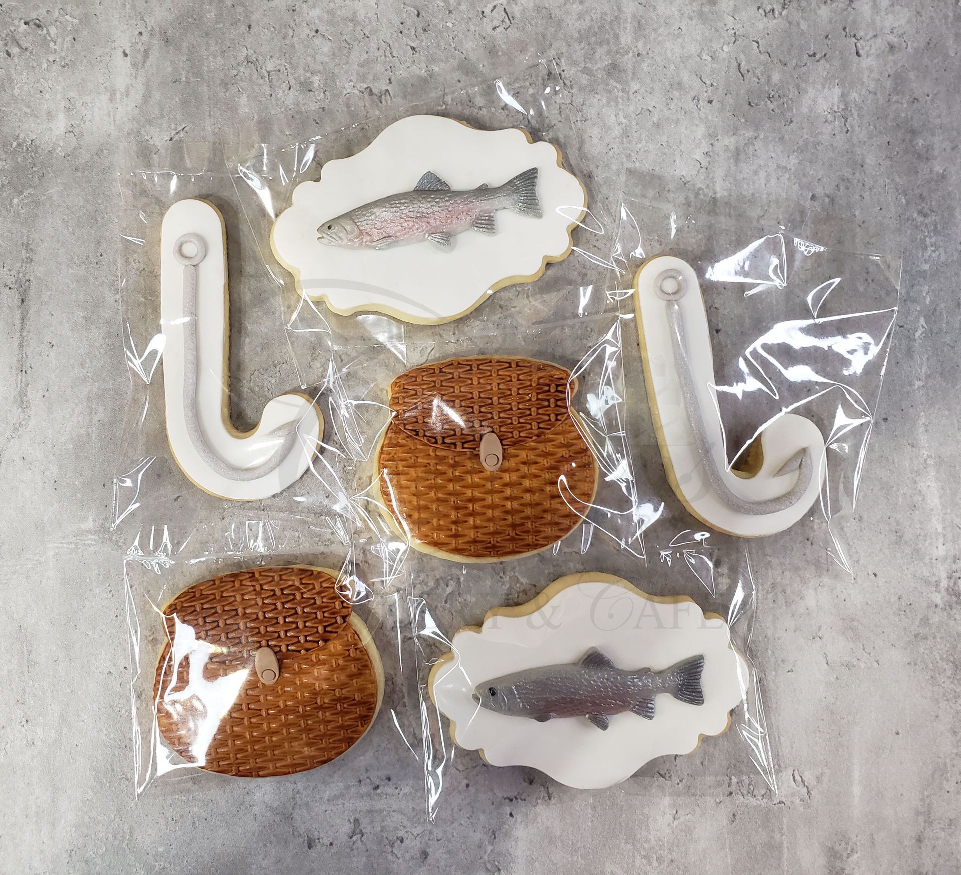 Assorted decorated cookie pops and sandwich cookies on clear wrappers over a gray surface