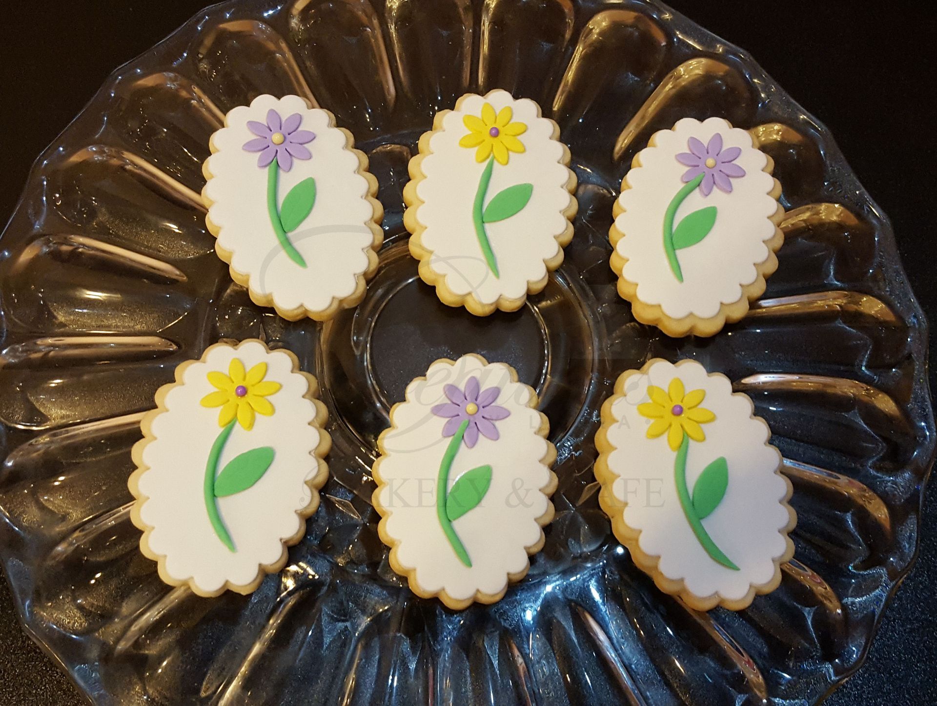 Decorated flower-shaped cookies with purple and yellow icing on a dark glass plate