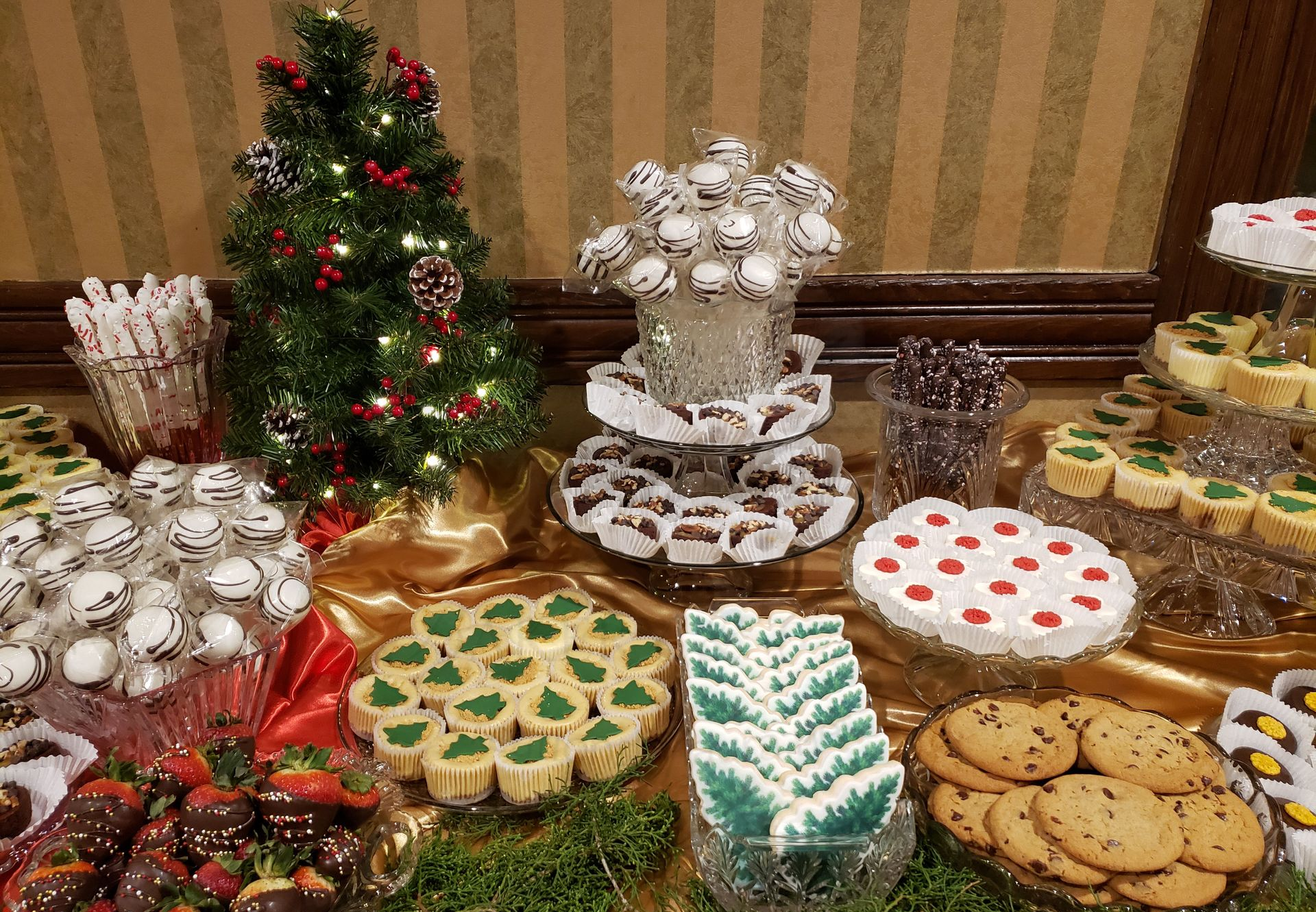 Assorted decorated holiday cookies and treats displayed on a table with small Christmas trees and festive decor