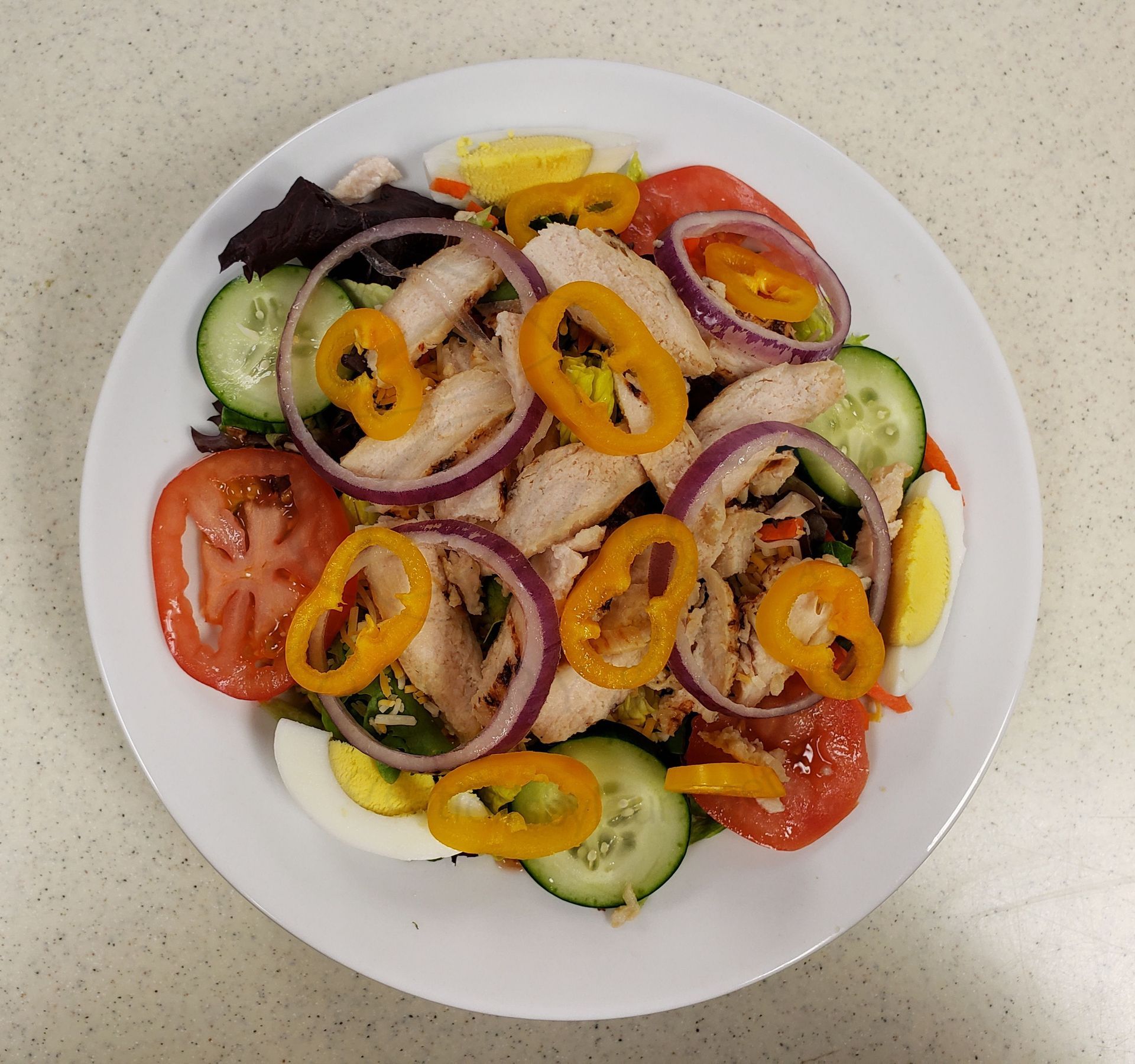 Salad with tomatoes, cucumbers, red onion, and yellow peppers on a white plate