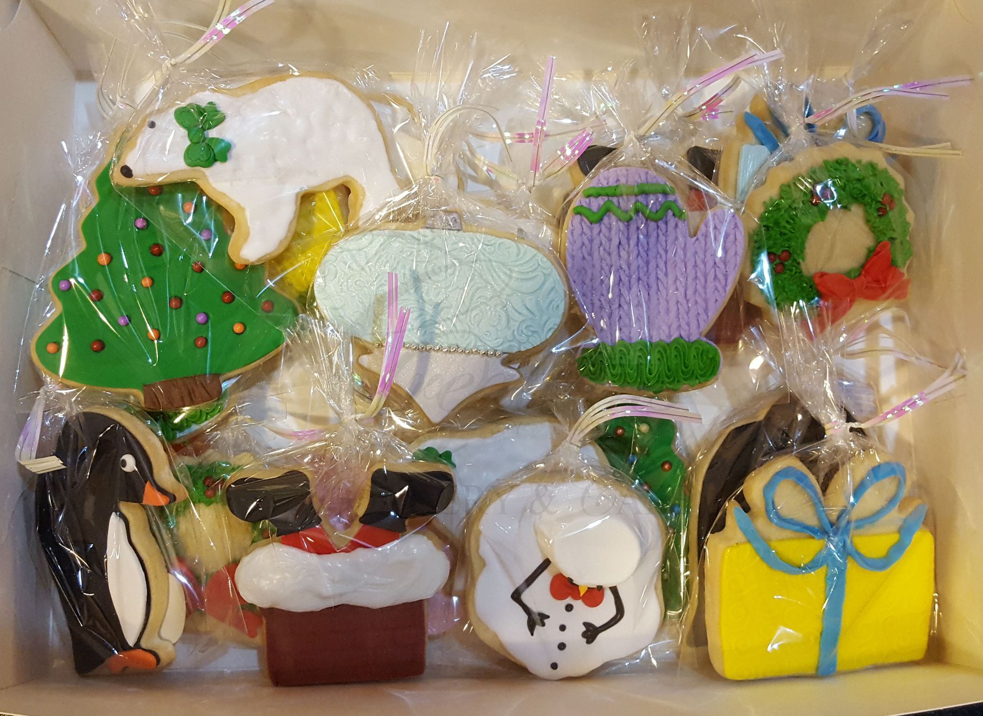 Assorted decorated holiday cookies wrapped in clear plastic, including a Christmas tree, penguin, mug, and gift box