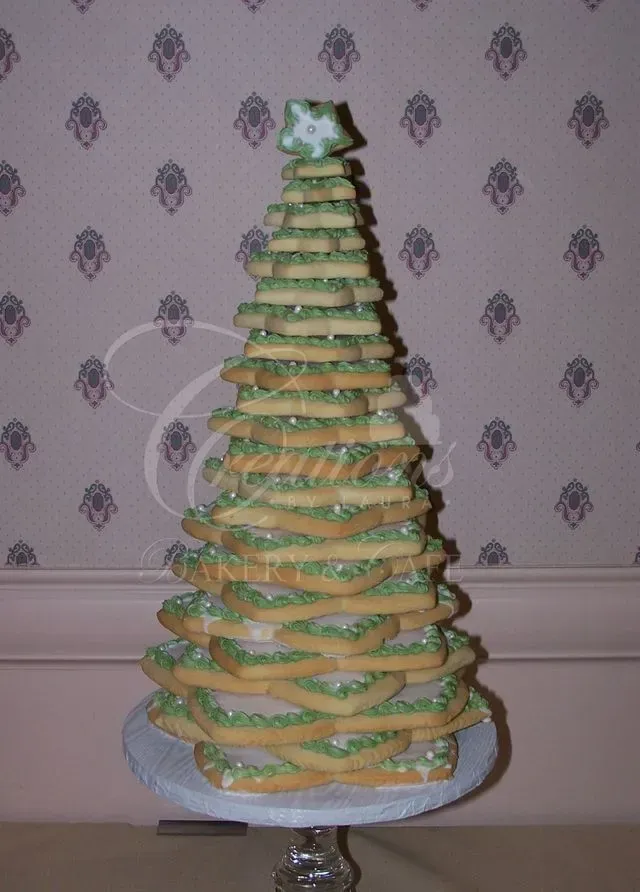 A tiered Christmas tree made of star-shaped cookies with green icing, standing on a pedestal against patterned wallpaper.