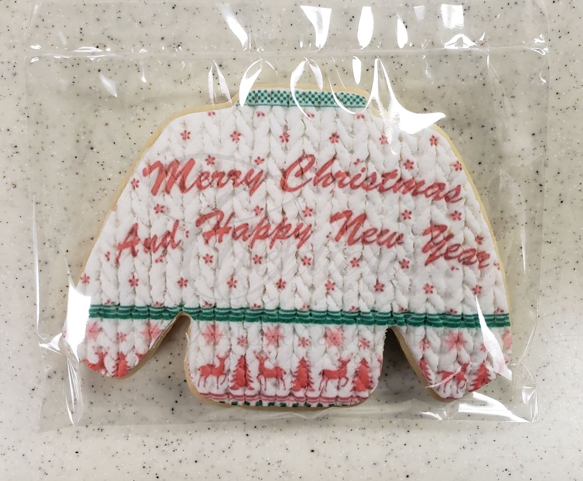 White Christmas sweater with red lettering and green trim, packaged in clear plastic on a speckled countertop