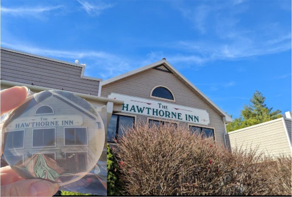 Hand holding a Hawthorne Inn keychain in front of the Hawthorne Inn building sign.