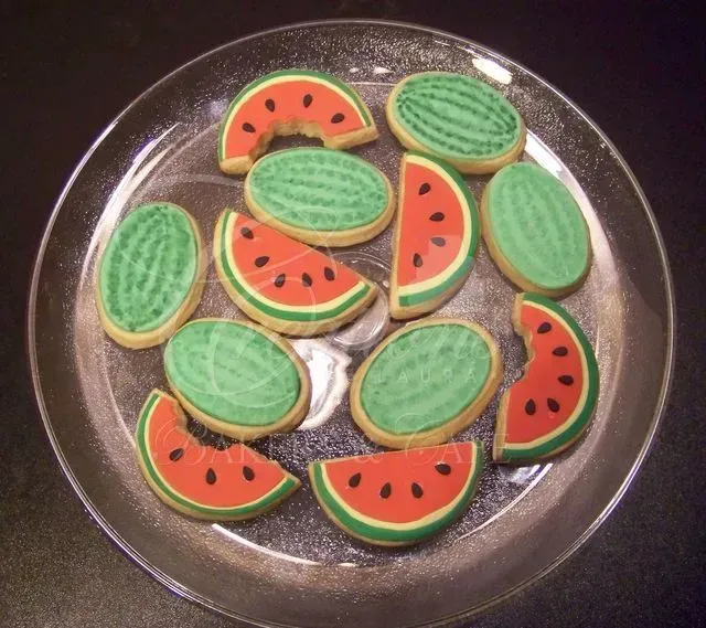 Plate of watermelon-shaped cookies with green and red icing on a glass dish