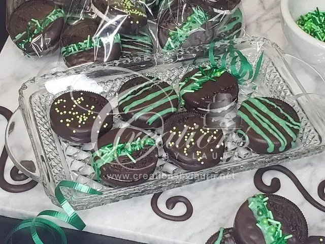 Tray of decorated chocolate cookies wrapped in clear plastic with green ribbon on a white patterned surface