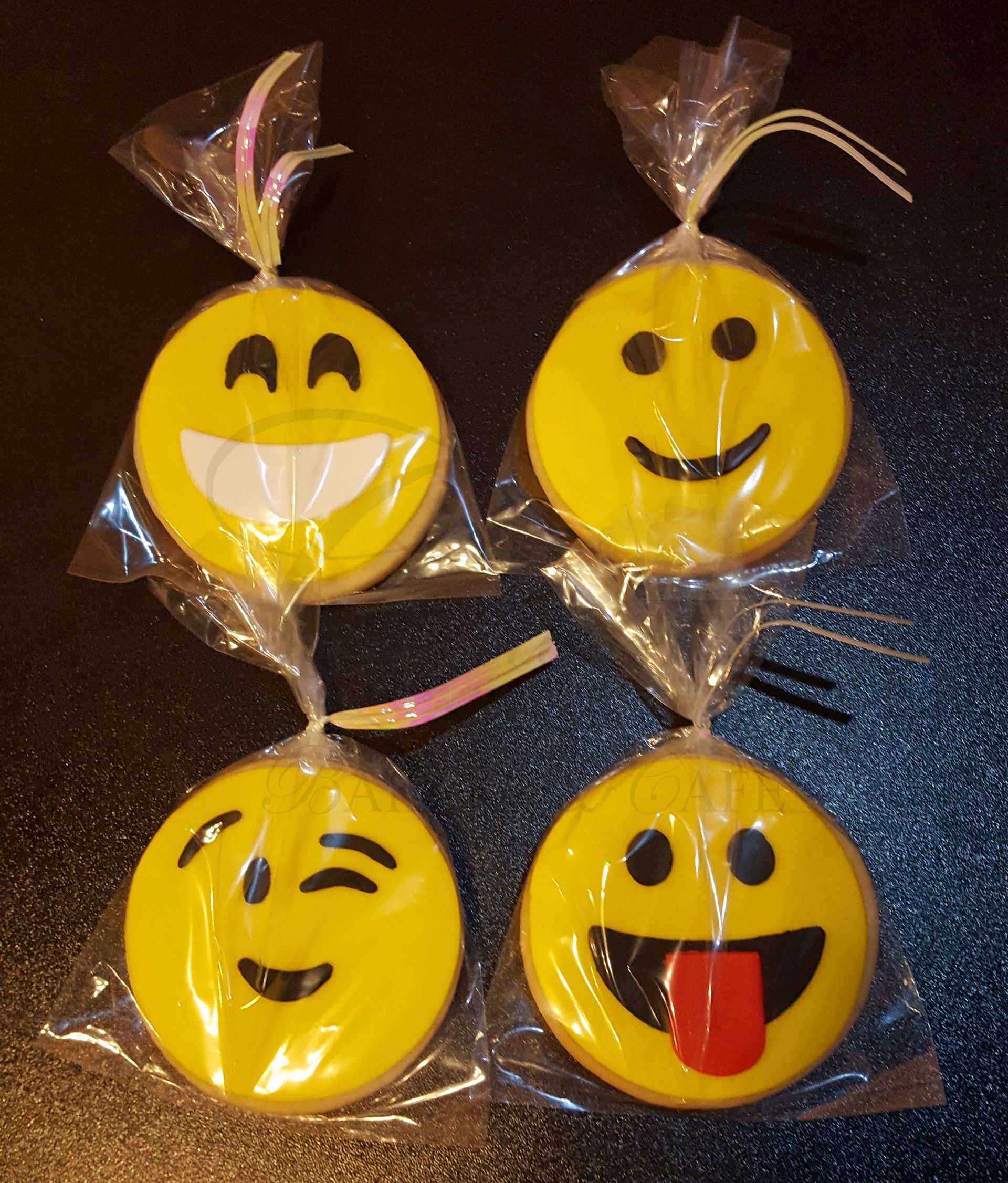 Four wrapped yellow smiley-face candies with different expressions on a dark surface.