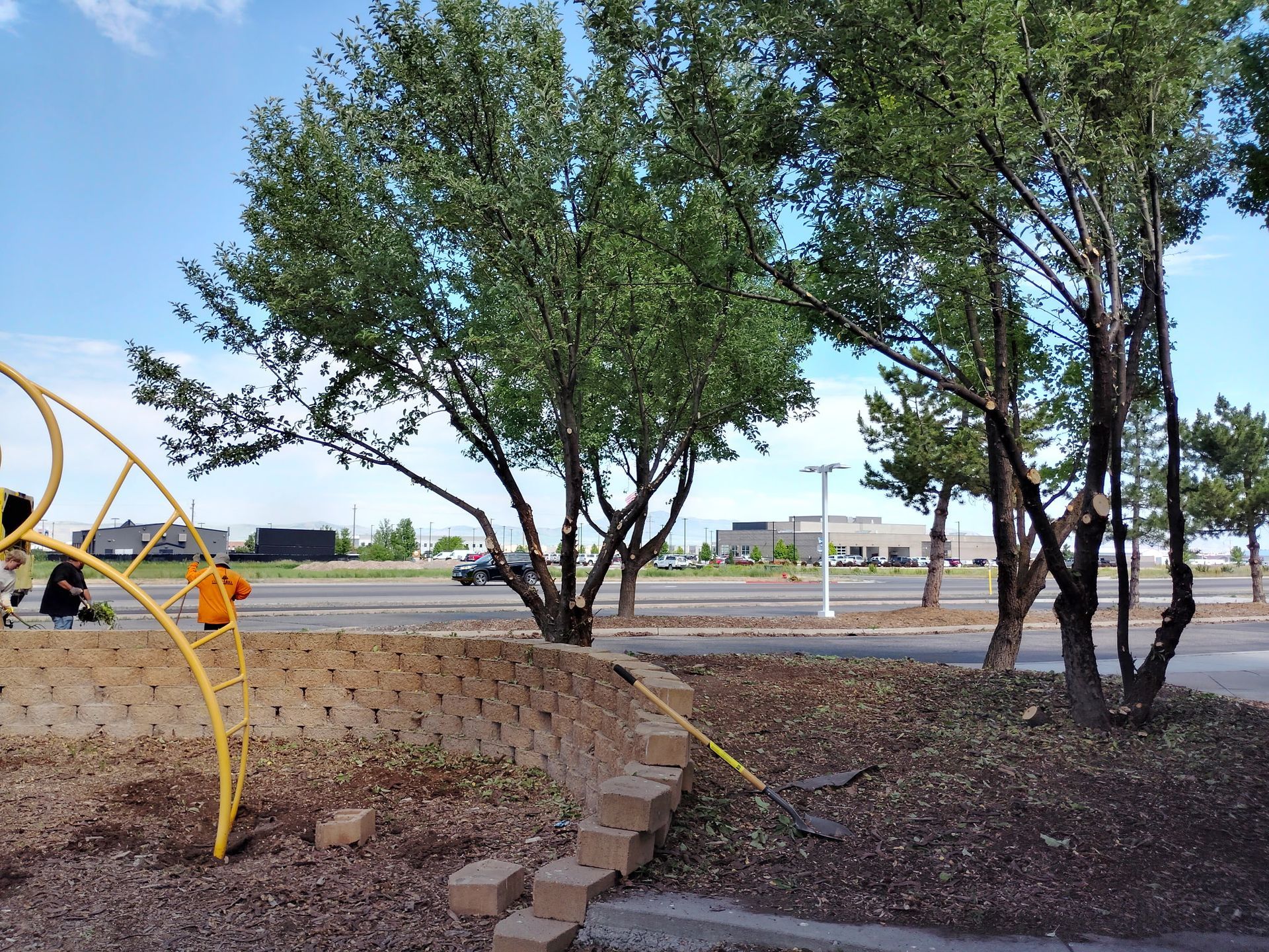 Trees and a dirt path by a playground under a clear blue sky with a distant road and buildings