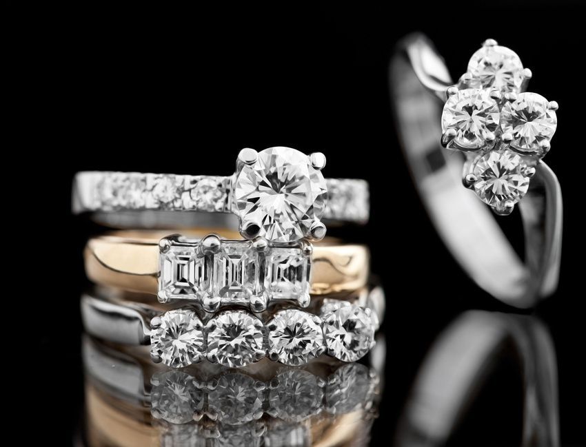 Pile of diamond rings in varying styles against a black background.