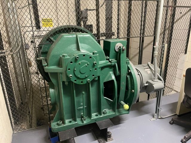 A green gearbox is sitting on the floor in an elevator.