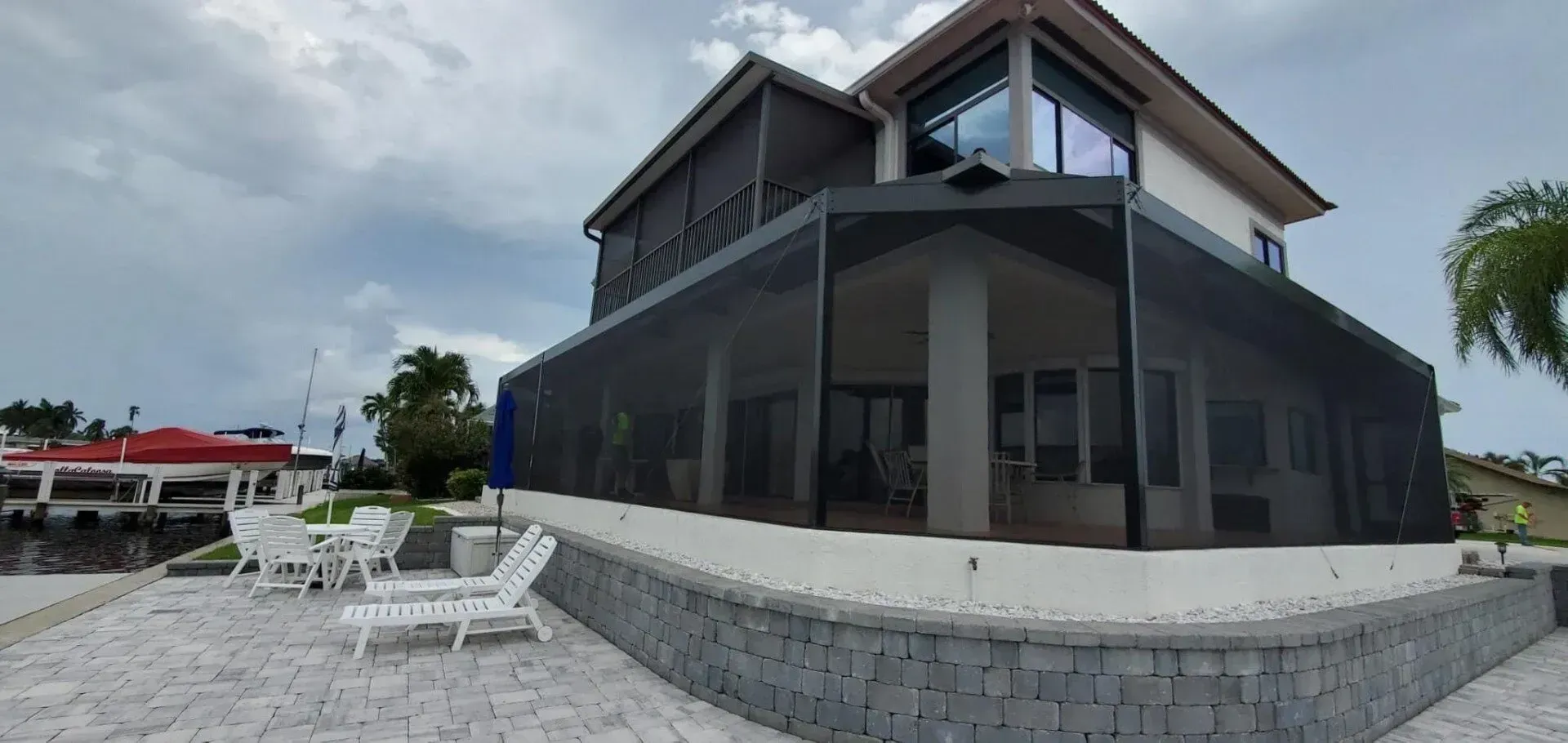 Exterior of a modern home with a screened-in porch, near a waterfront, with white patio furniture.