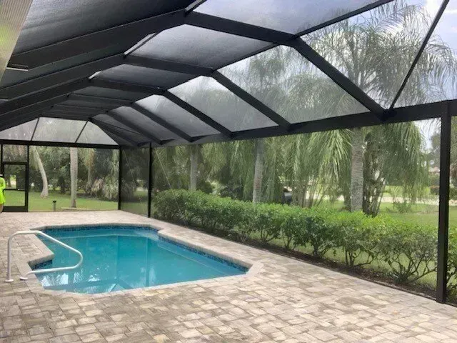 Pool enclosure with a pool, brick floor, and lush green background.