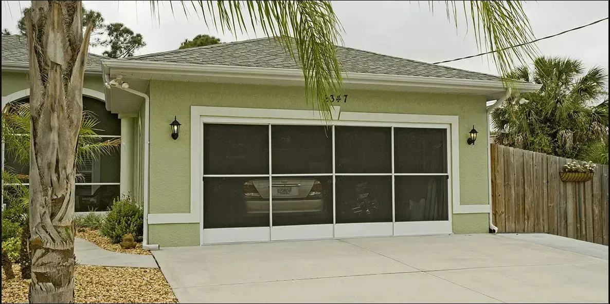 House with a screened garage door and a concrete driveway, surrounded by vegetation.