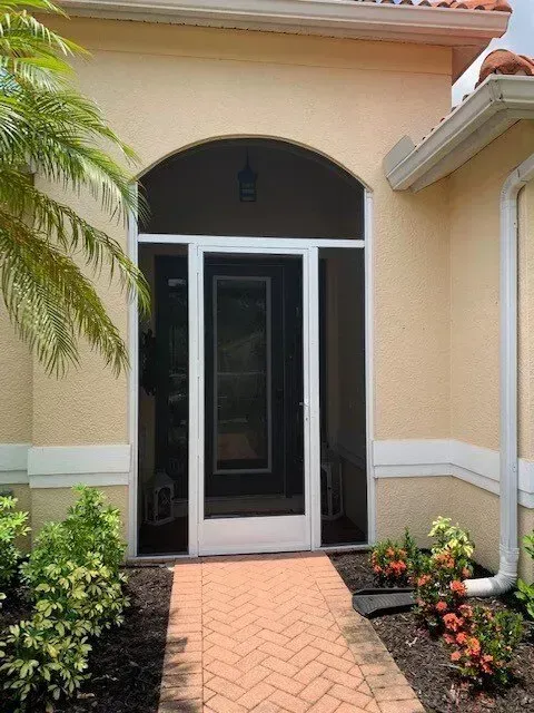Front entrance with arched entryway, screen door, brick pathway, and landscaping.