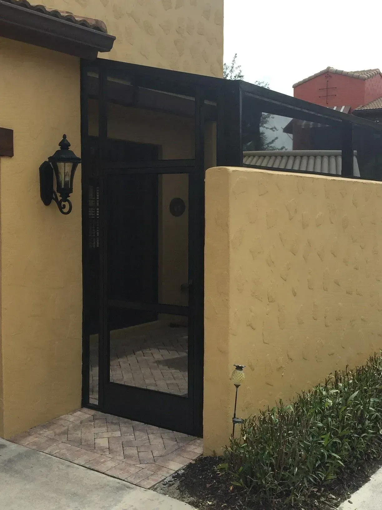 Black gate and glass entry framed by stucco walls. Brick path leads to the door.