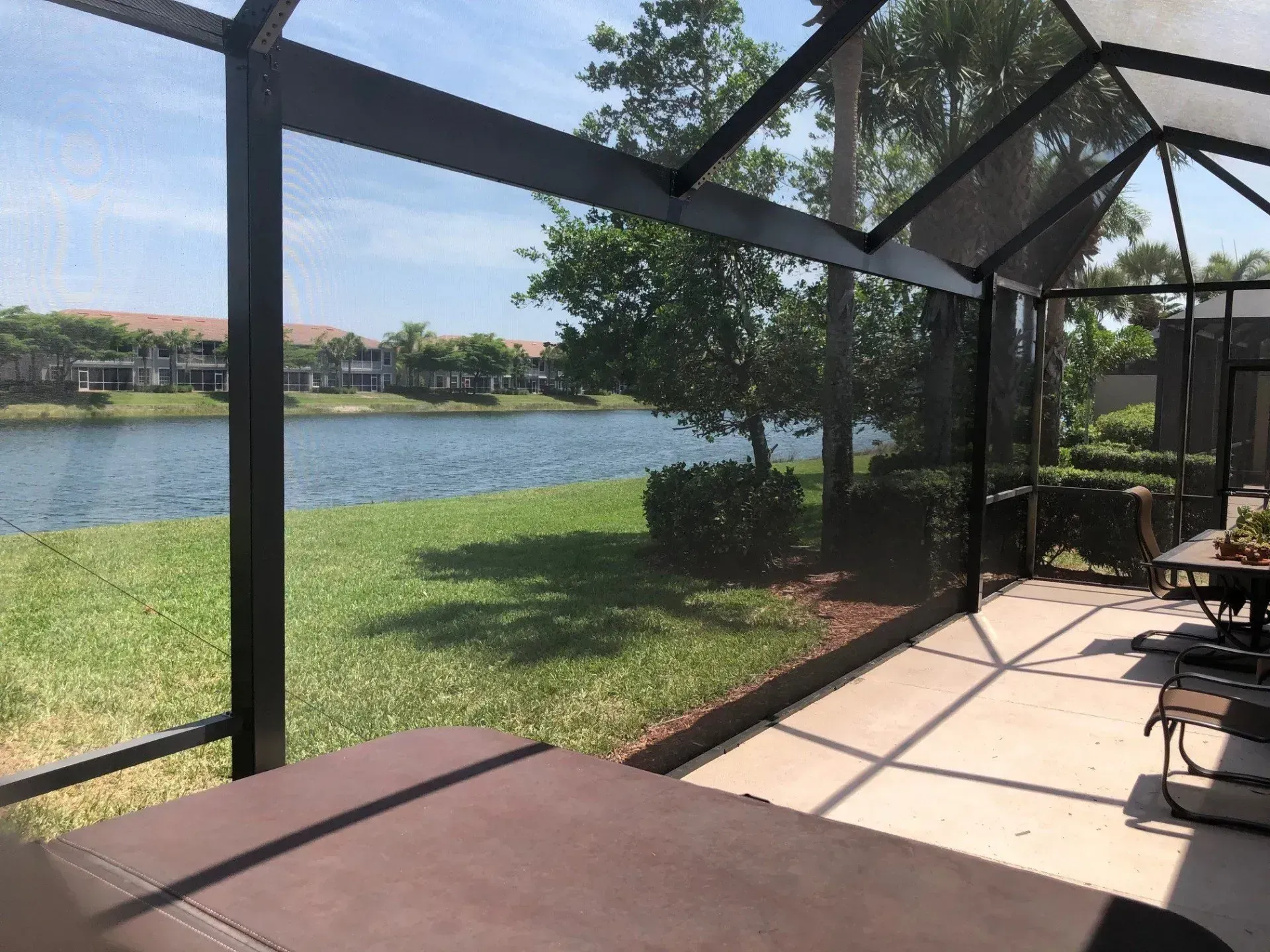 Screened patio overlooking a lake and grassy yard, with visible patio furniture and nearby houses.