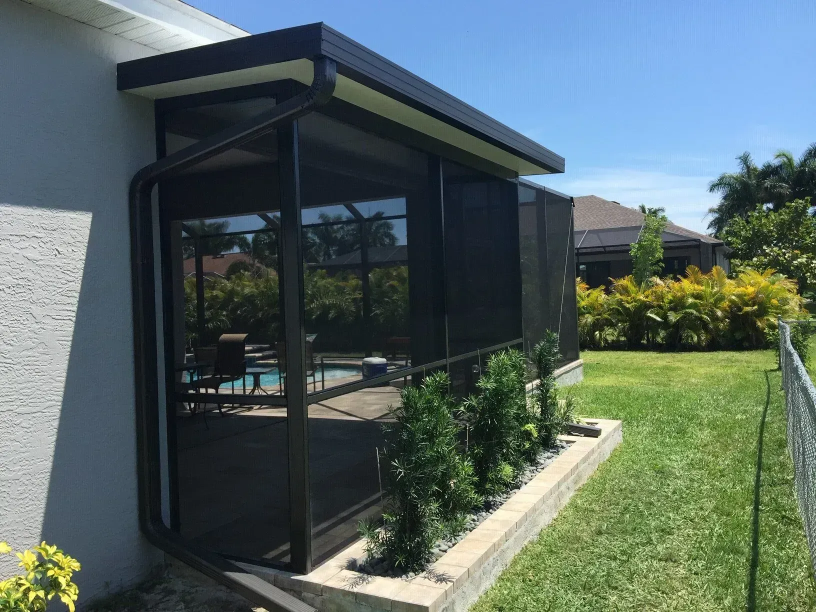 Screened-in patio extension attached to a house with a pool view, black framing and a green lawn.