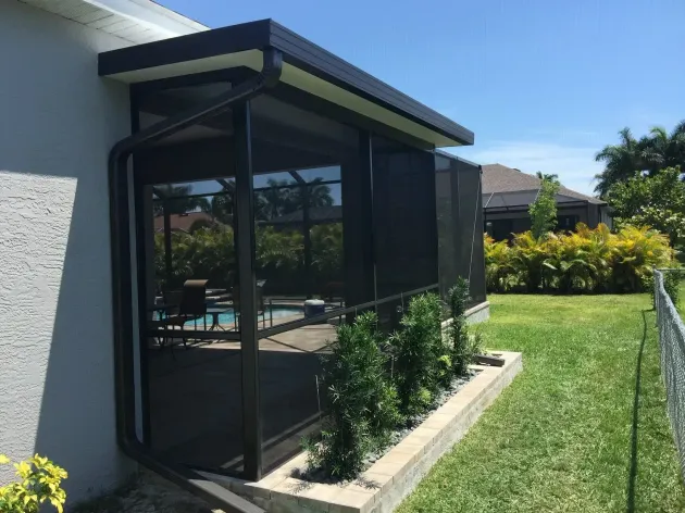 Screened-in patio extension attached to a house with a pool view, black framing and a green lawn.