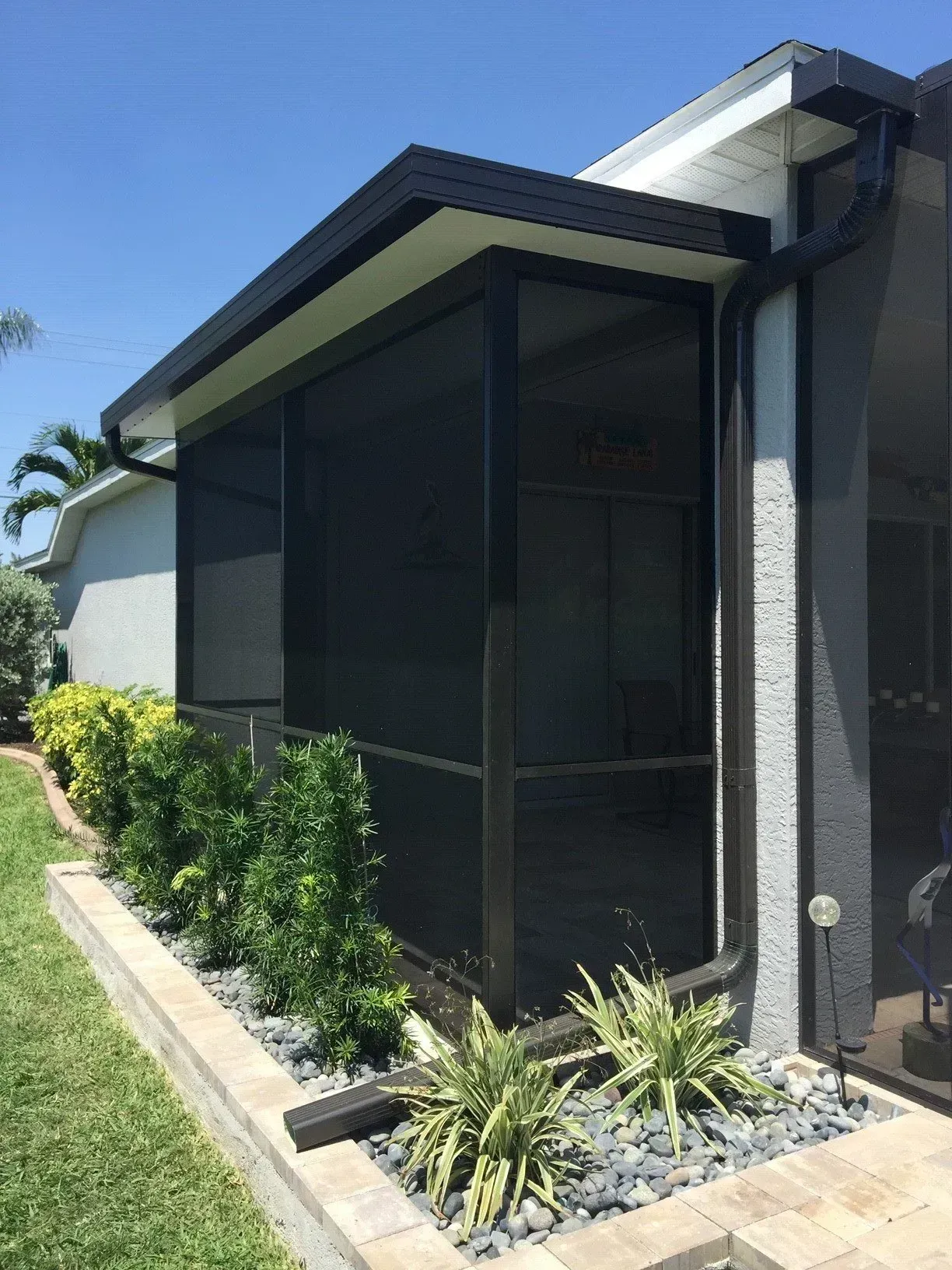 A screened porch extension with black screens and trim, next to a house with black gutters.