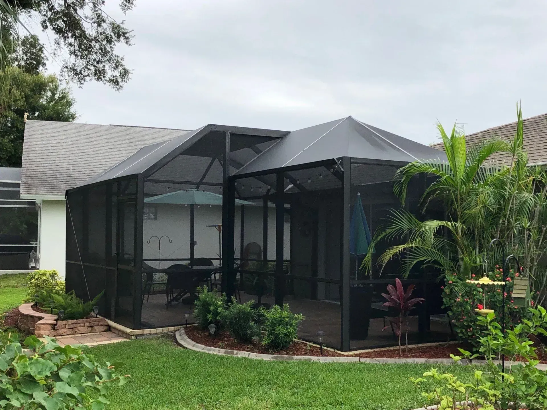 Screened patio with black frame, dark roof, and lush landscaping.