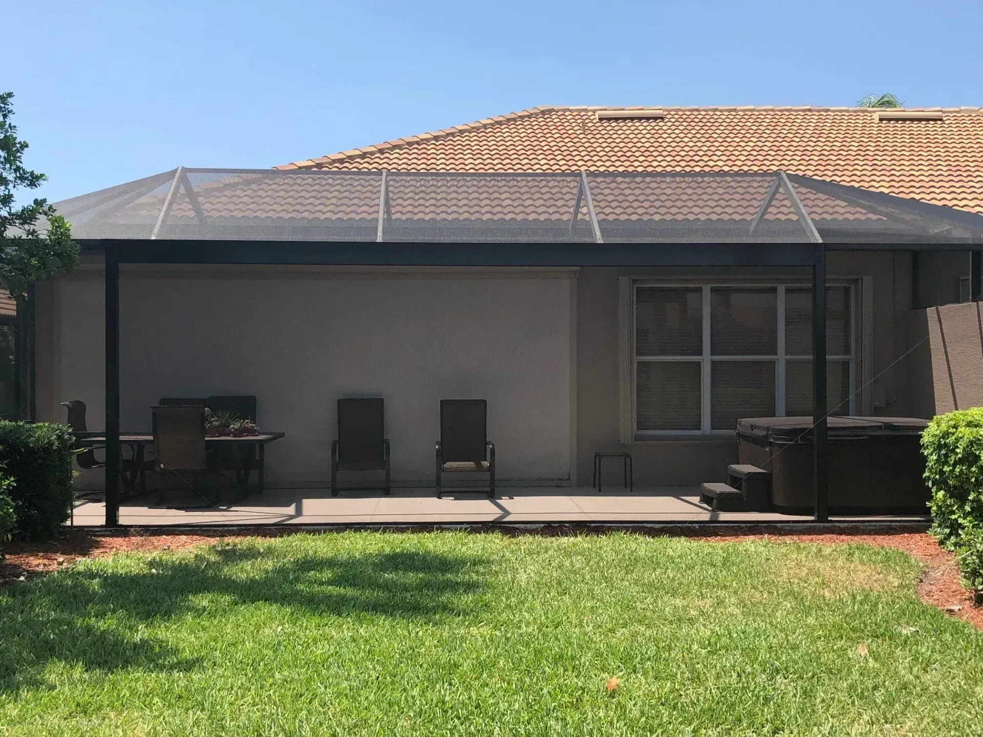 Patio with screen enclosure; chairs, table, and hot tub visible; sunny day.