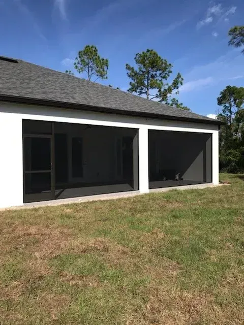 Screened patio attached to a white house with gray roof, set on a grassy lawn.