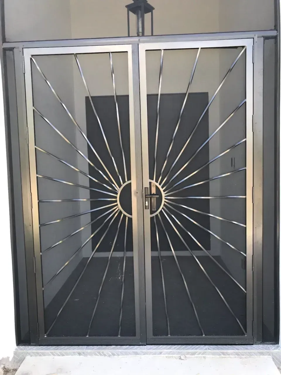 Double metal security doors with sunburst design, gray mesh, and circular handle.